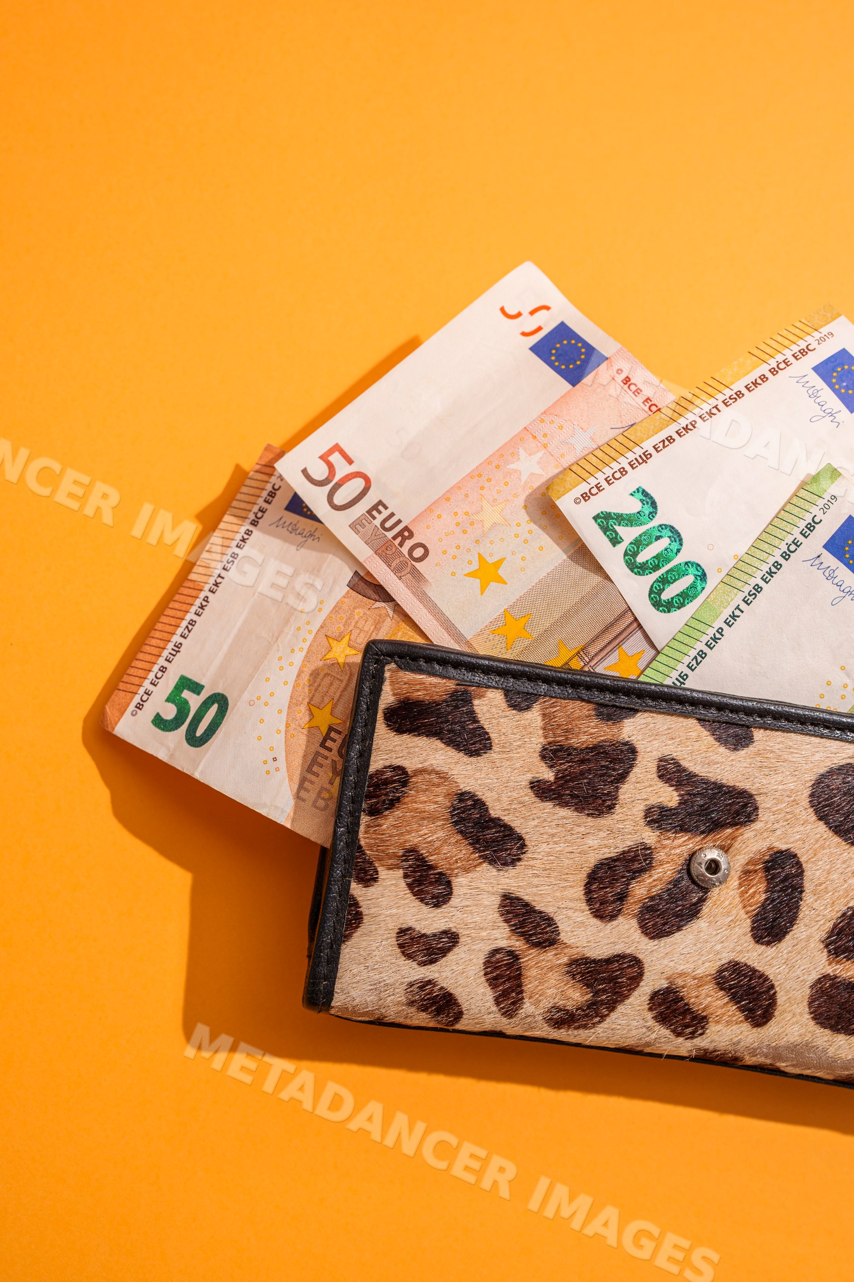 Leopard print wallet with euro banknotes on orange background