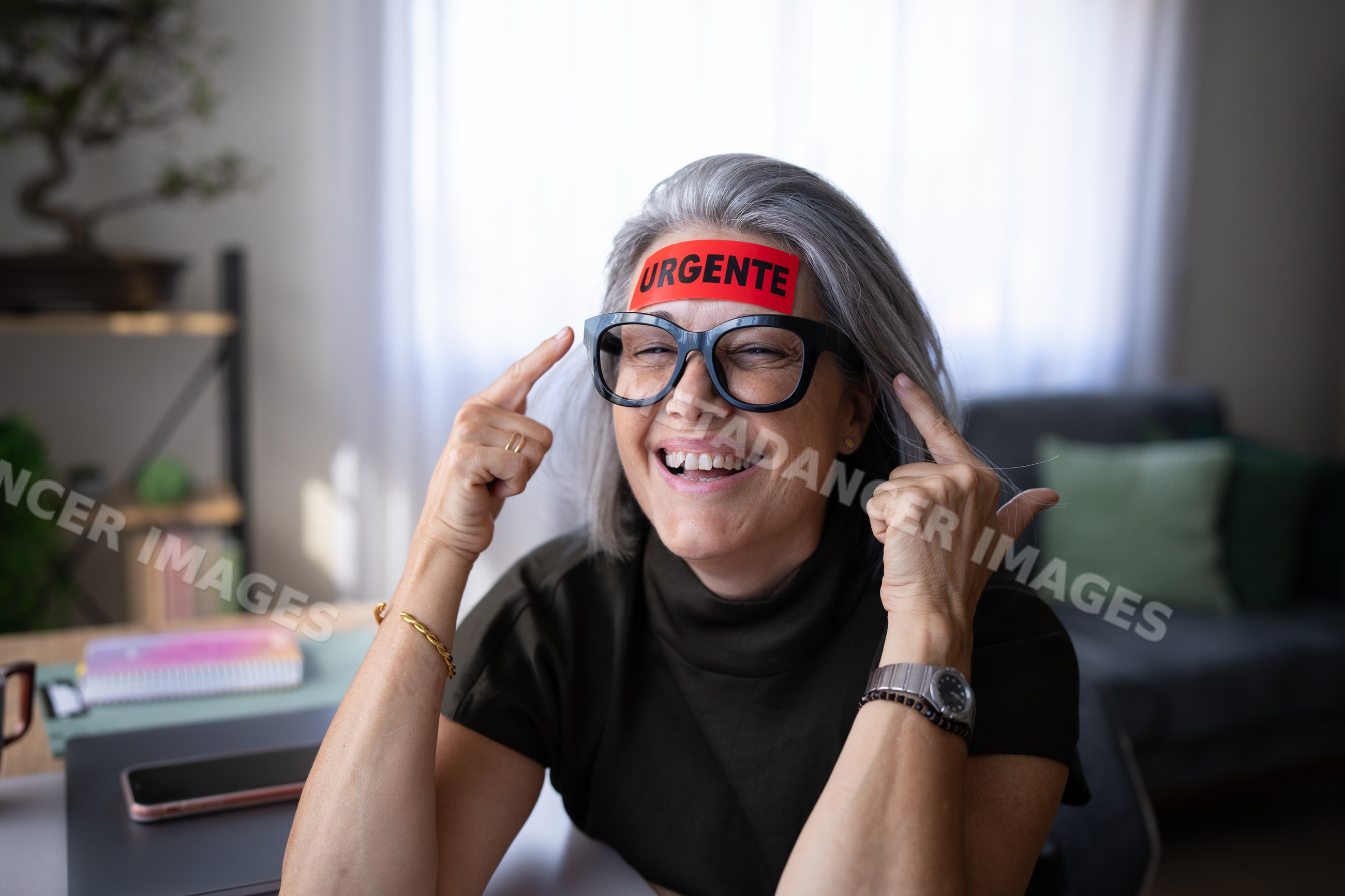 White woman smiling with urgent sticker on forehead in home office