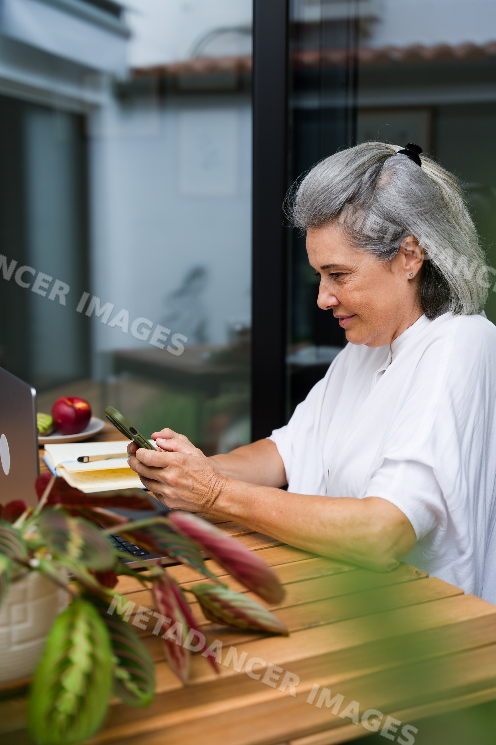 White Woman using smartphone at wooden table with laptop and notebook