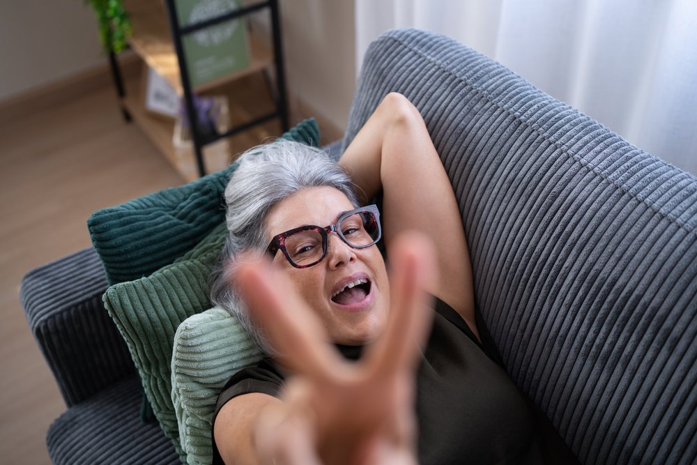 White woman relaxing on sofa making victory gesture at home