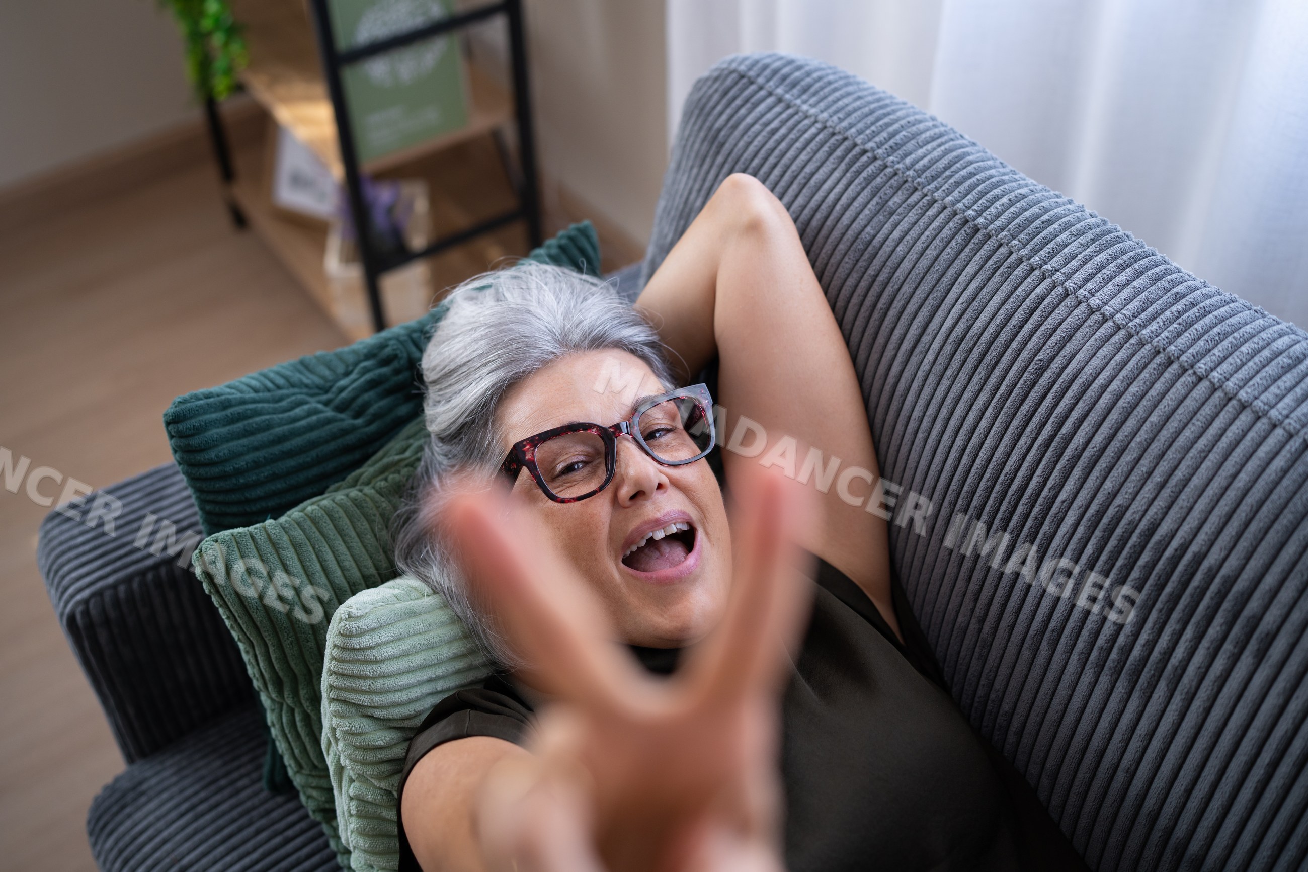White woman relaxing on sofa making victory gesture at home