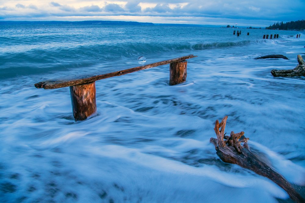Ocean waves surrounding wooden plank on seashore