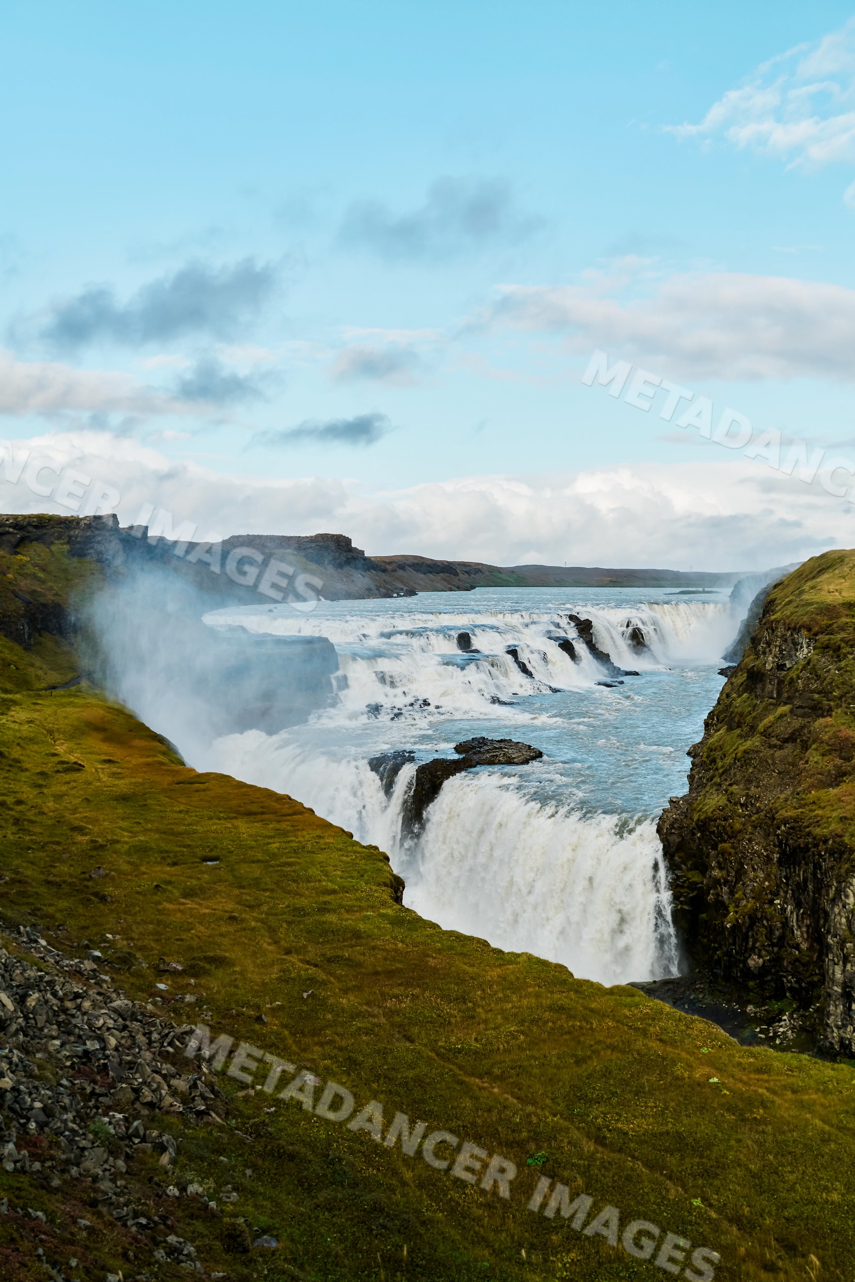 A cascading waterfall flows through rocky cliffs and grasslands
