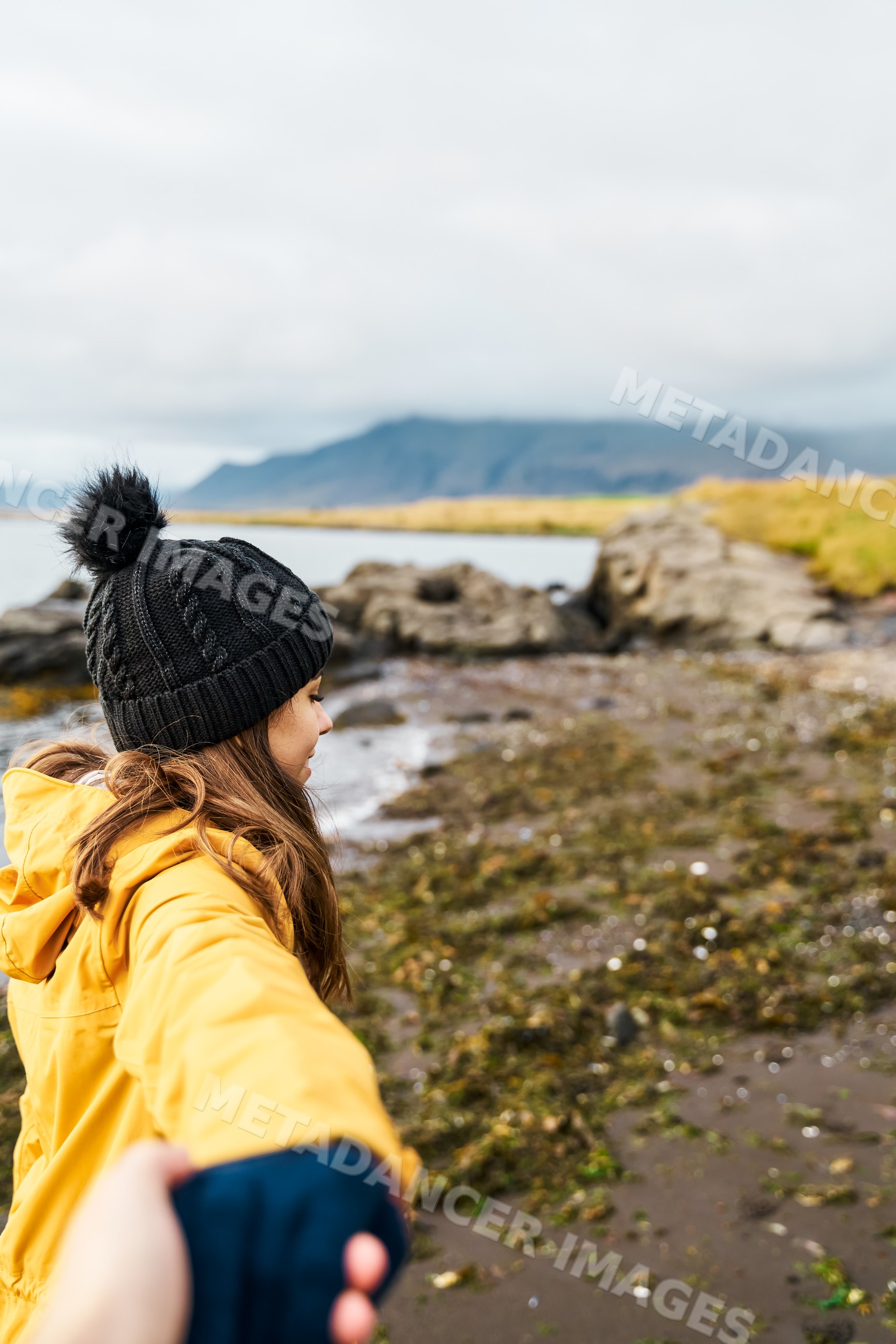A white woman holding a hand walks along a rocky shoreline