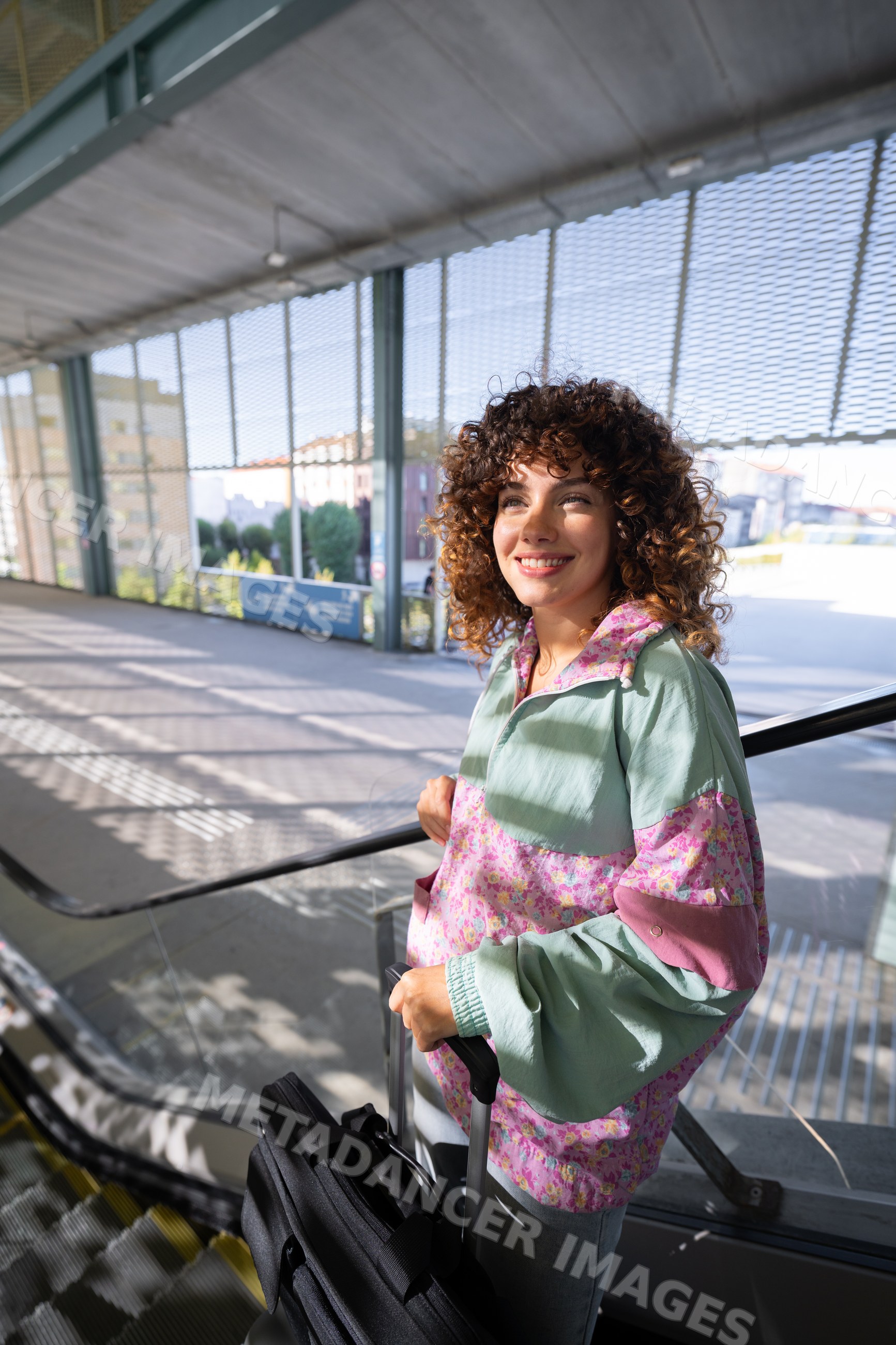 White woman holding luggage on escalator in urban outdoor setting