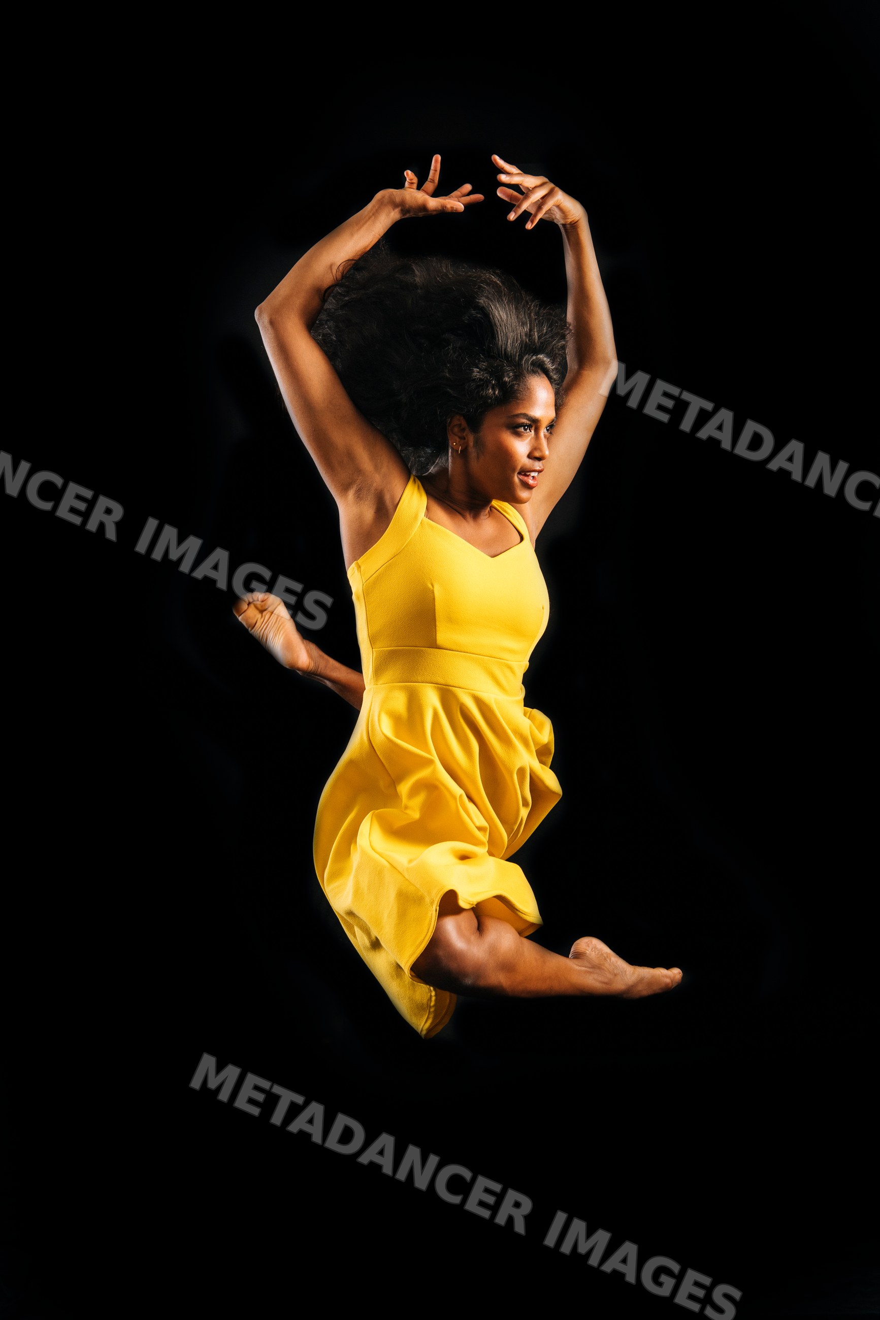 South Asian woman jumping in yellow dress against dark background
