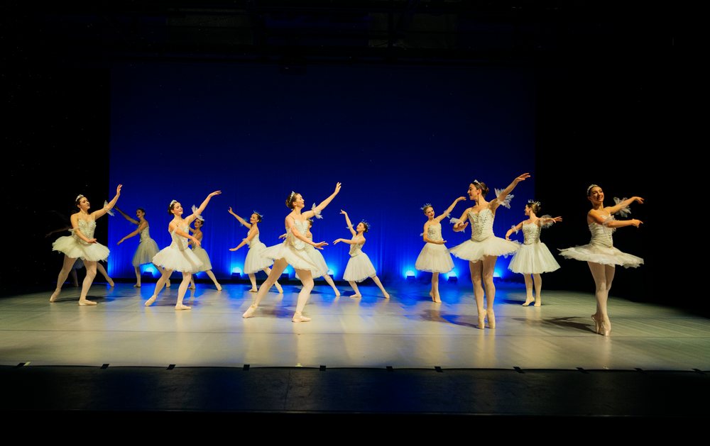 Ballet dancers perform a holiday-themed ballet on stage in white tutus