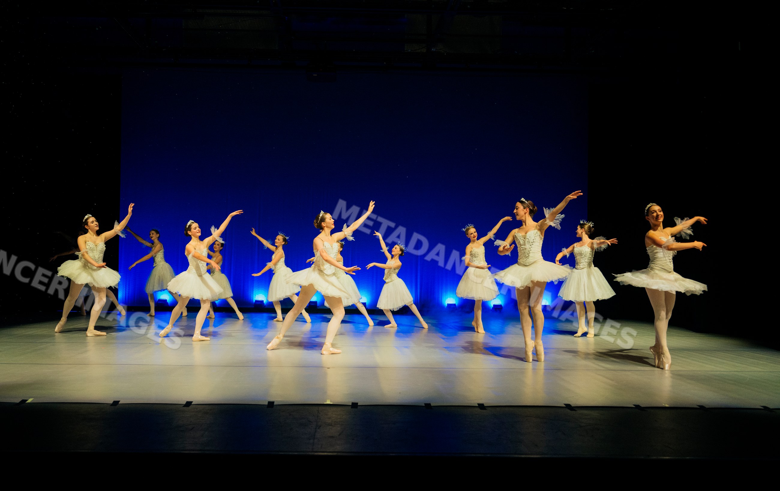 Ballet dancers perform a holiday-themed ballet on stage in white tutus