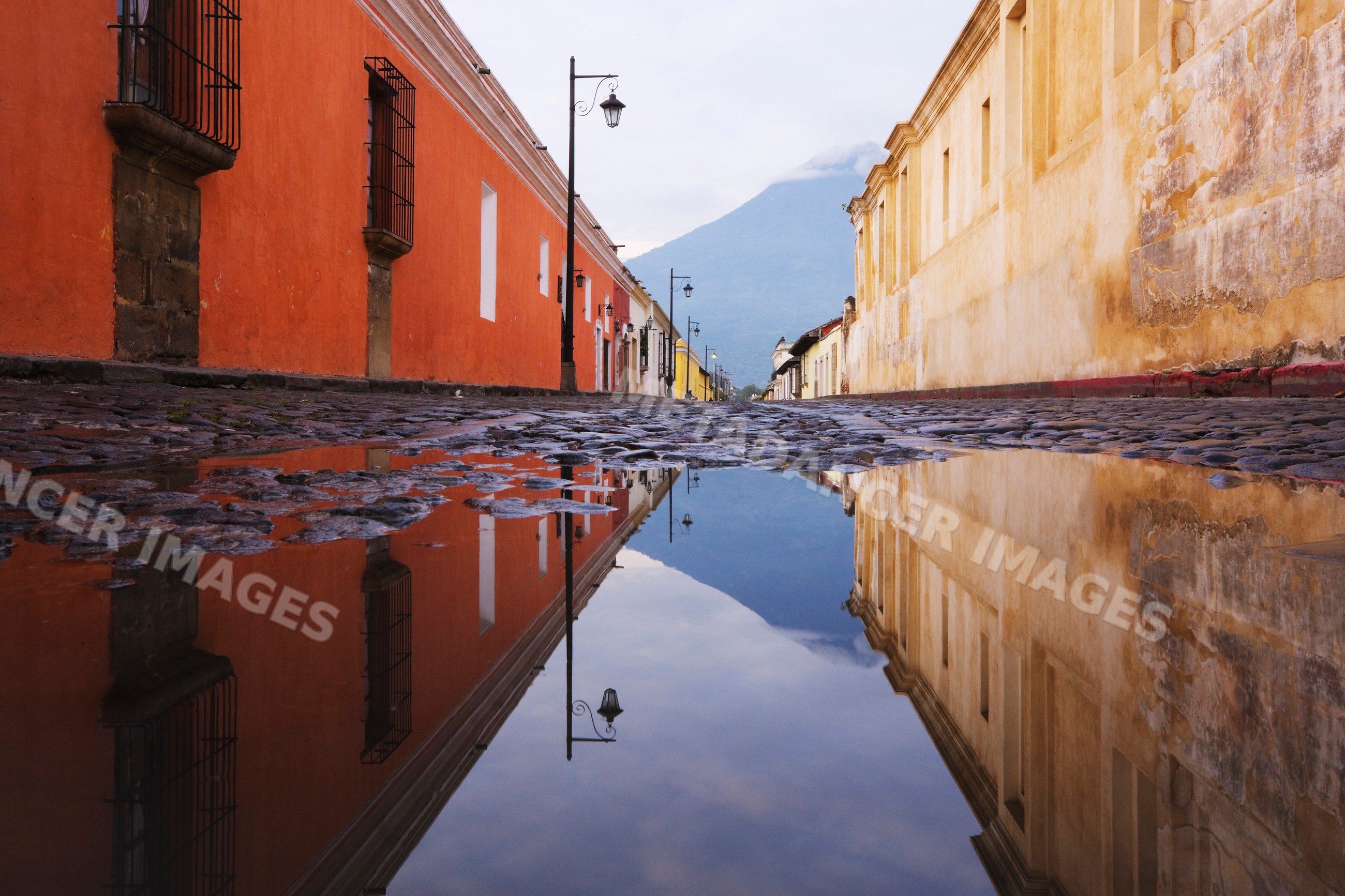 Street with reflective puddle and distant volcano, guatemala