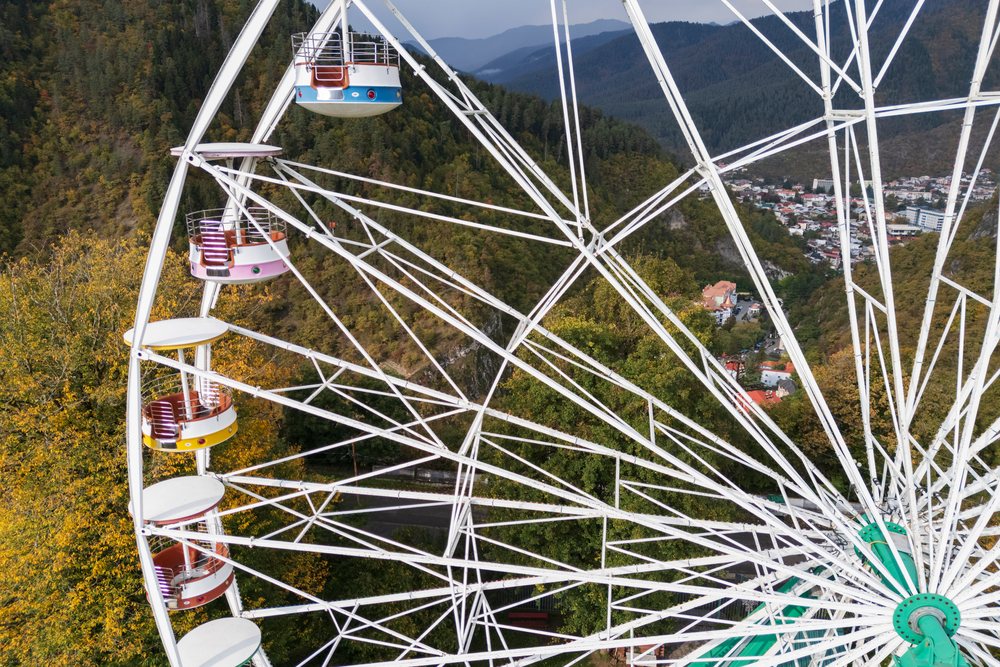 Ferris wheel and cable car above forested mountains and town
