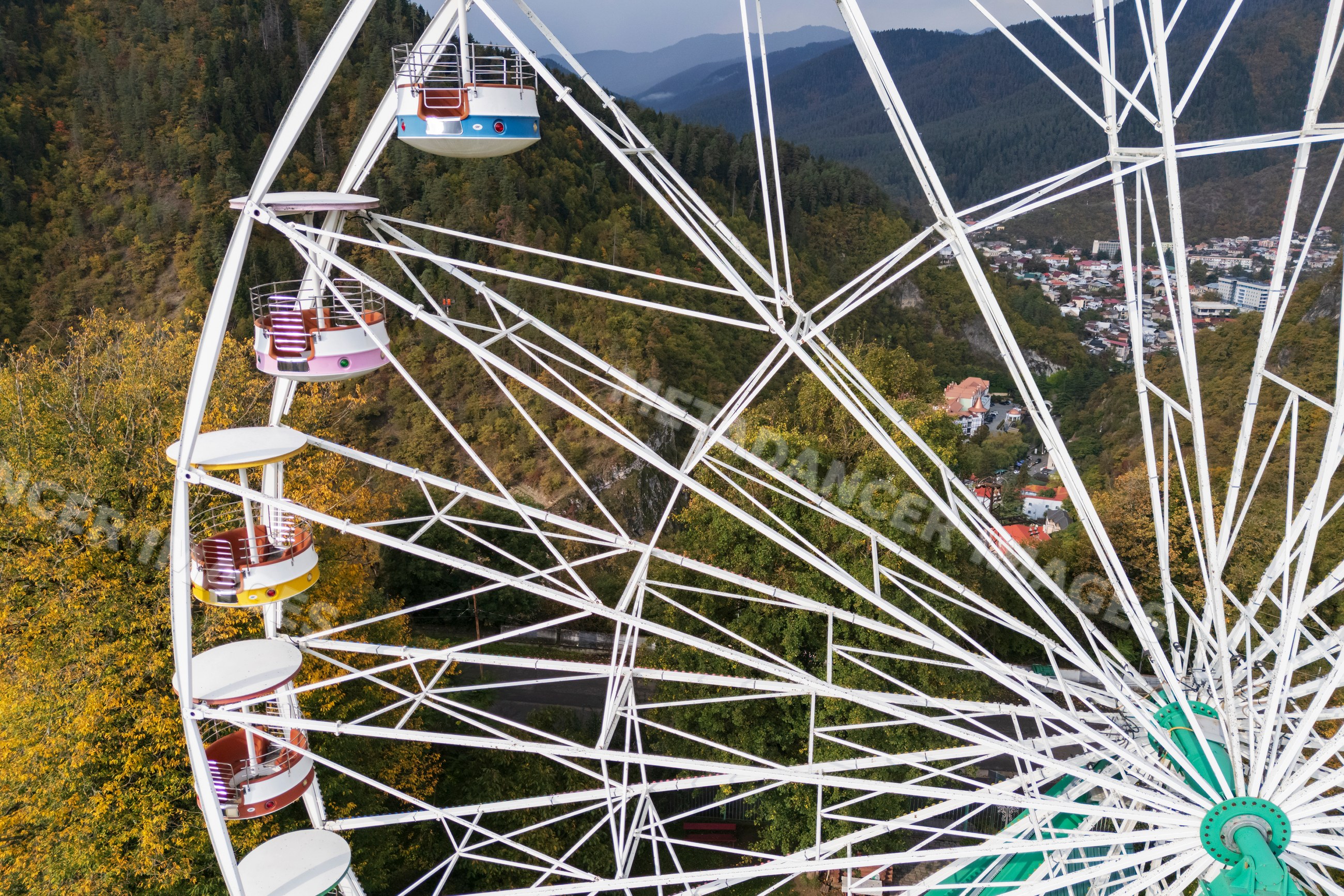 Ferris wheel and cable car above forested mountains and town