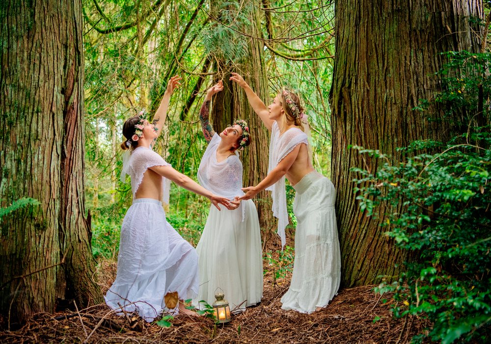 White women dancing with flower crowns in forest among tall trees