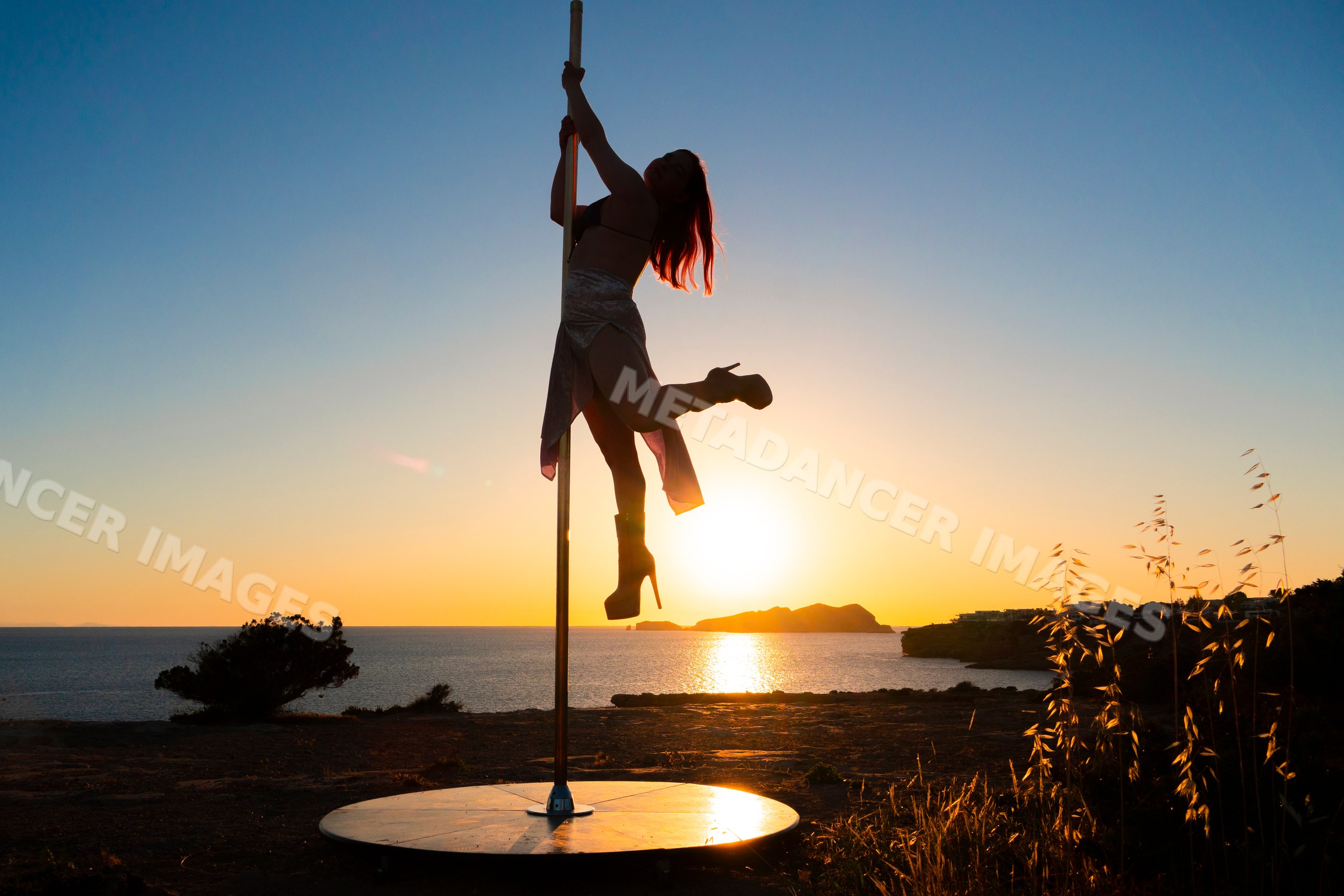Female Pole Dancer performing at sunset by Ibiza coastline