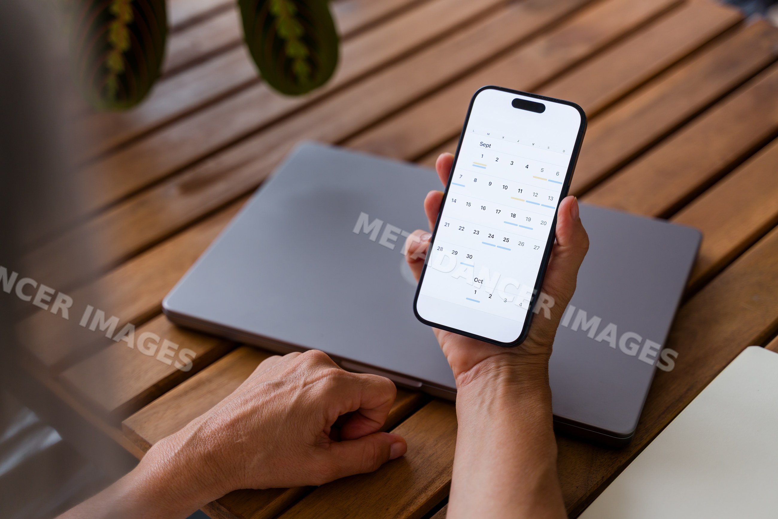 Hand holding smartphone with digital calendar on wooden table
