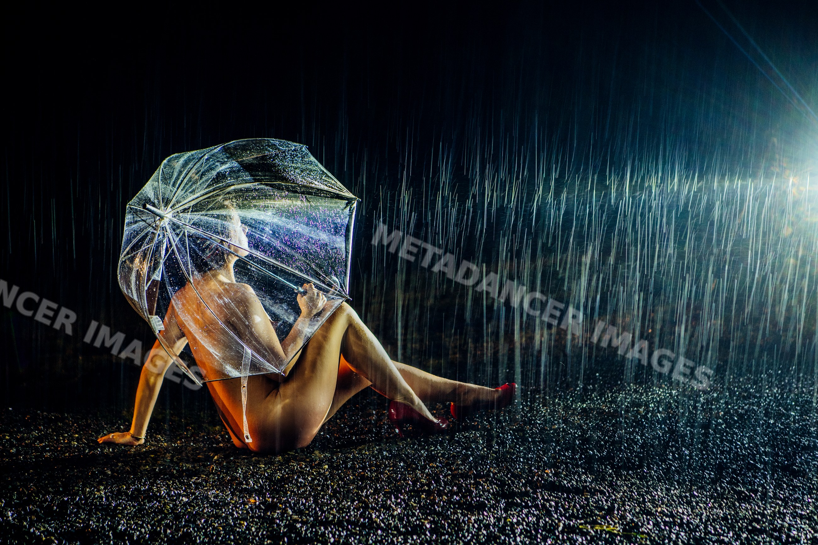 Nude white woman sitting in rain under transparent umbrella at night