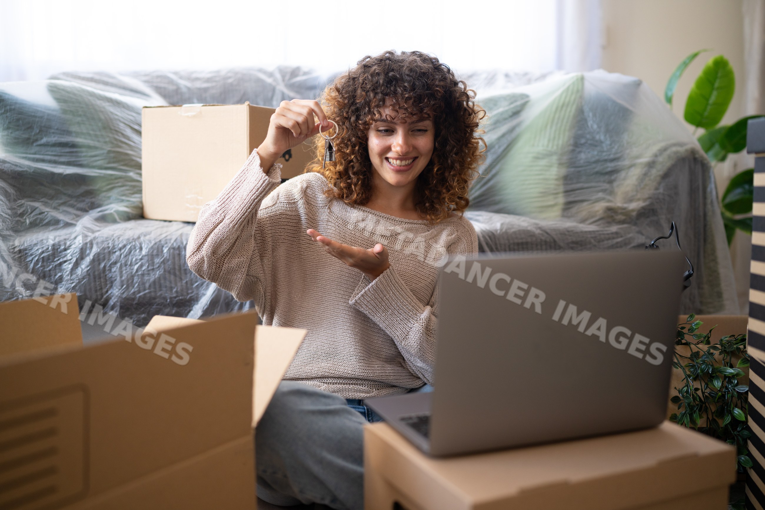 White woman holding keys smiling at laptop during home move