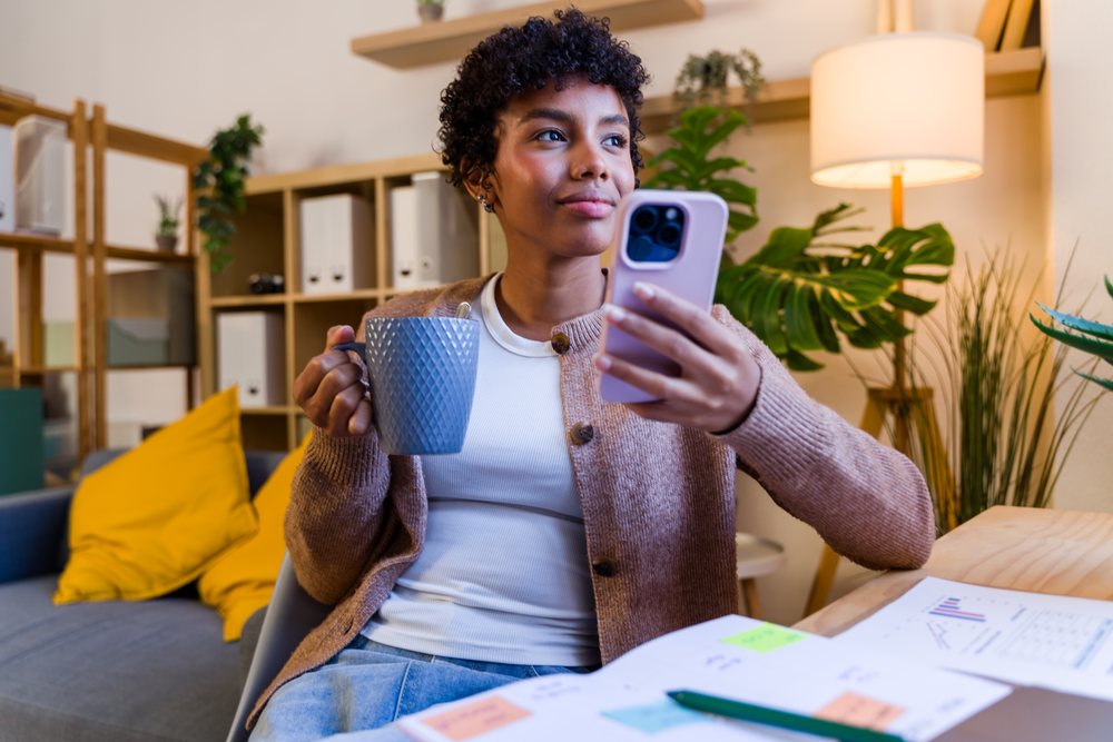 Young African American woman holding mug and using smartphone