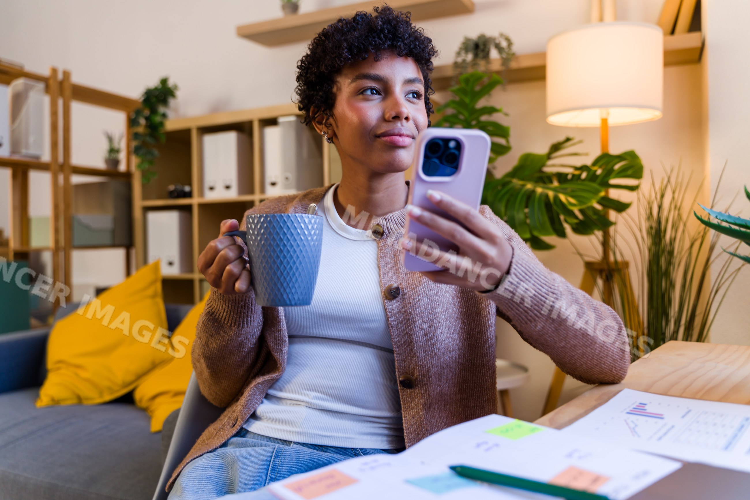 Young African American woman holding mug and using smartphone