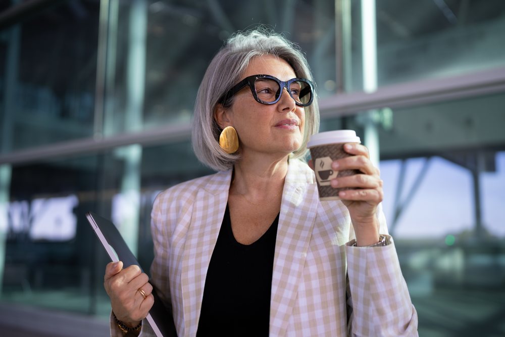 Businesswoman holding coffee cup and laptop outside modern building