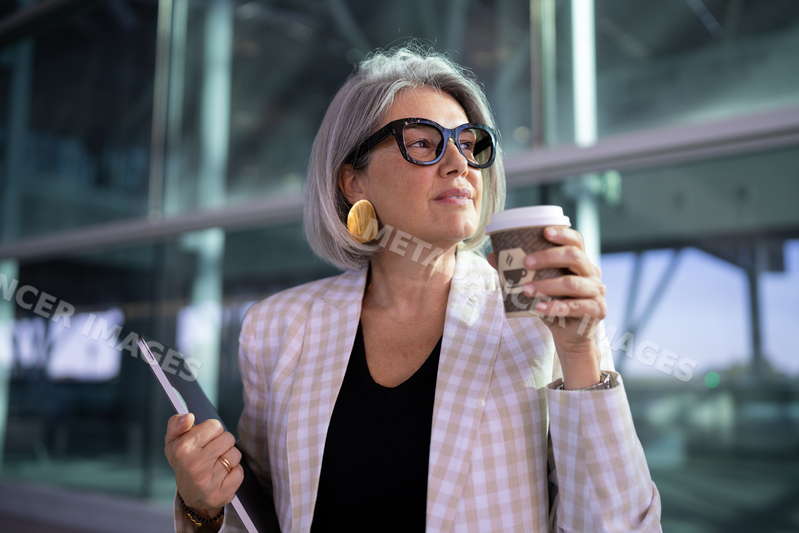 Businesswoman holding coffee cup and laptop outside modern building
