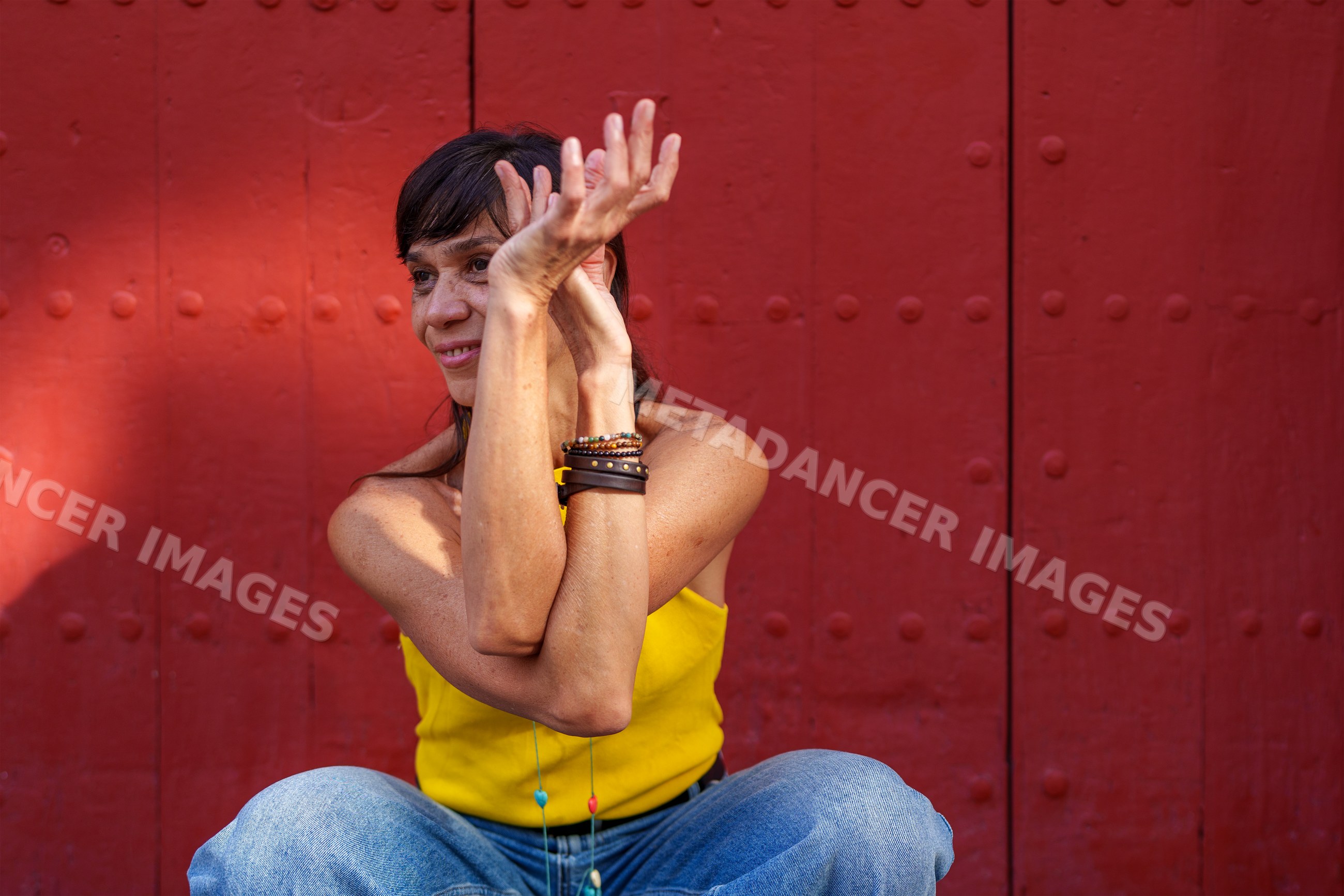Hispanic woman posing in yellow top and blue jeans by red door