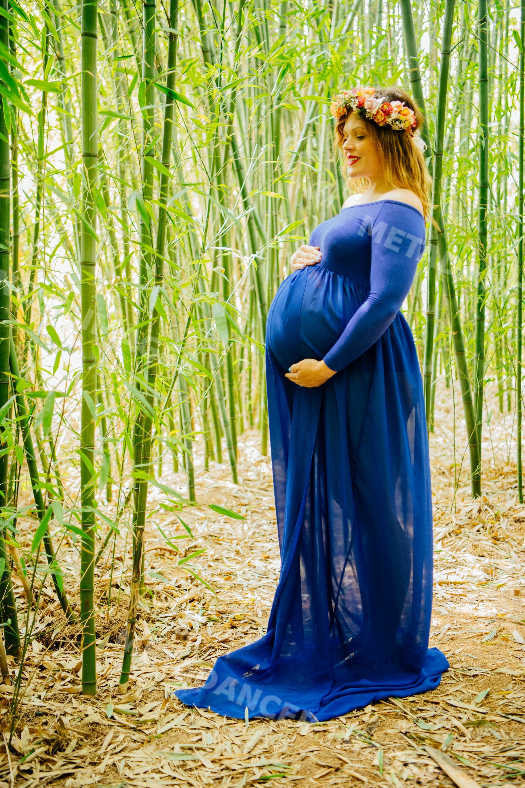Pregnant white woman in a blue dress standing in bamboo forest