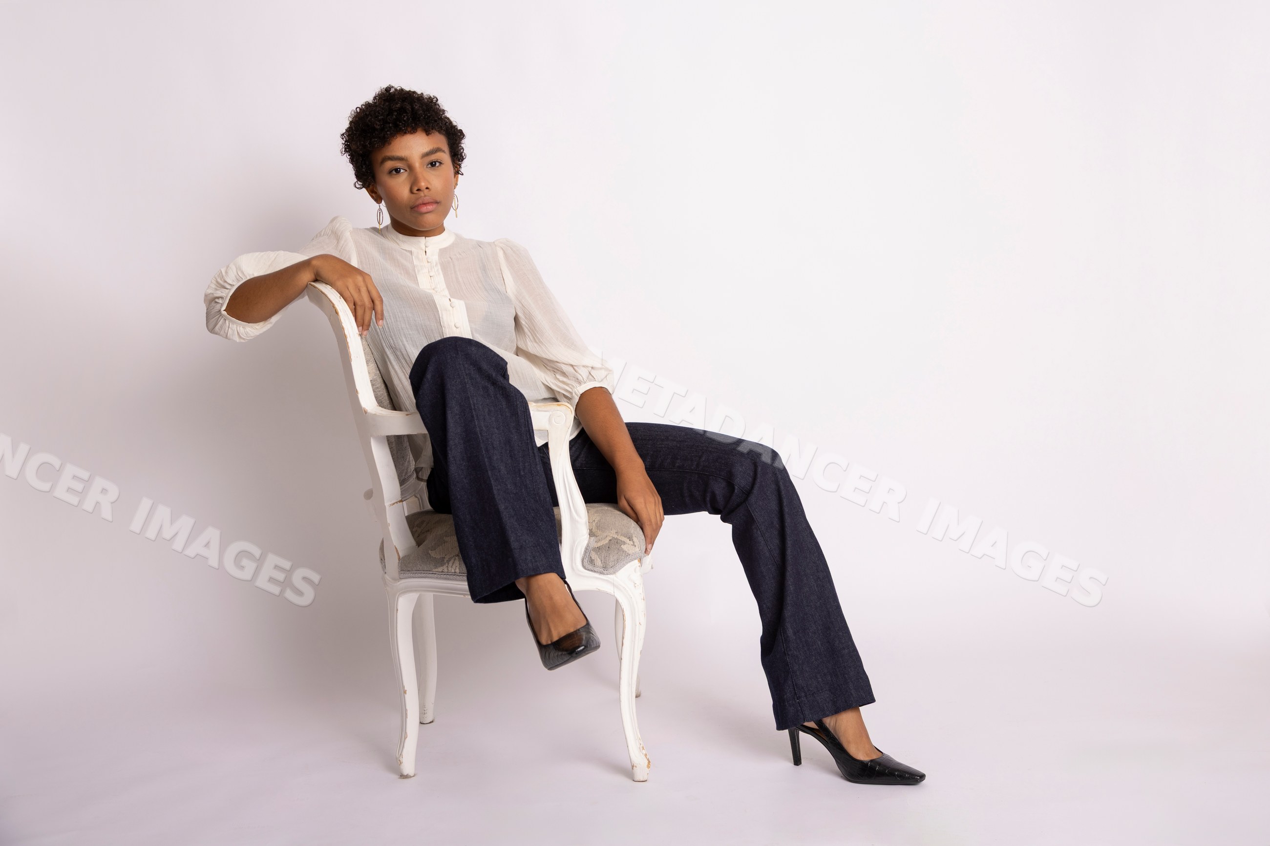 Hispanic woman in white blouse and dark jeans sitting on chair