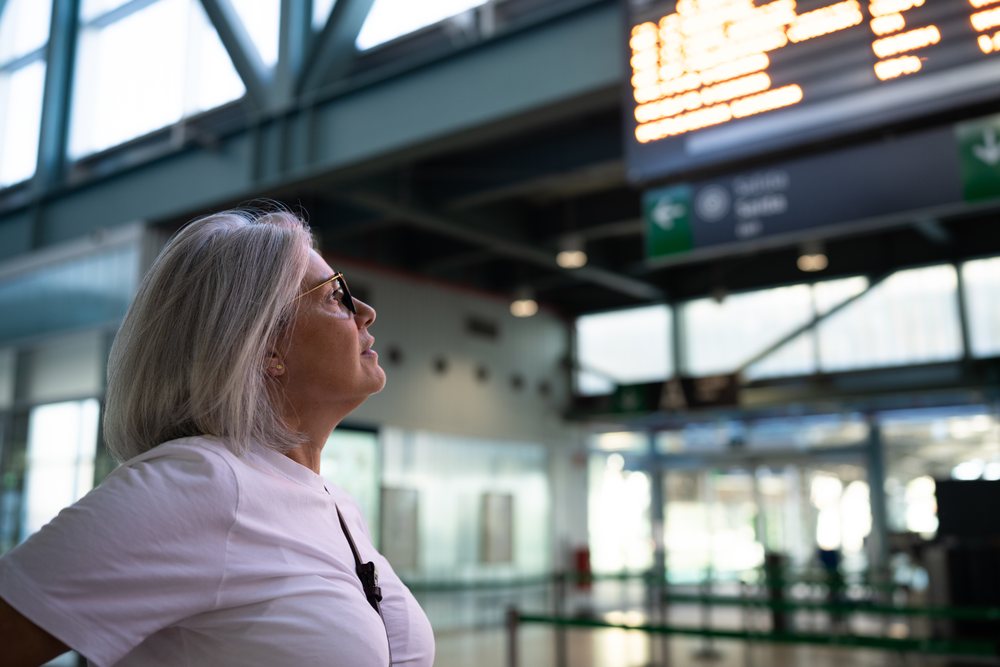 White woman looking at the departure board inside airport terminal