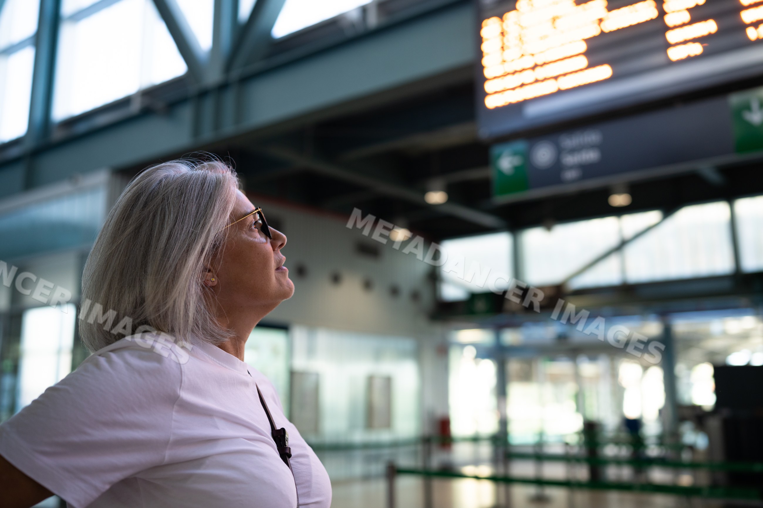 White woman looking at the departure board inside airport terminal
