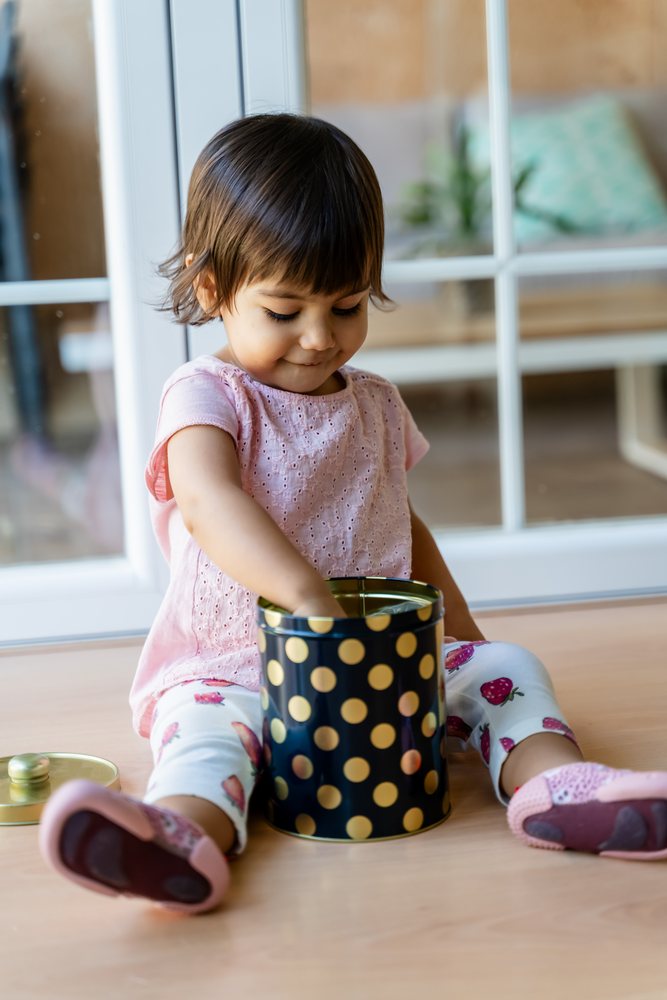 Toddler white girl playing with gold polka dot tin indoors