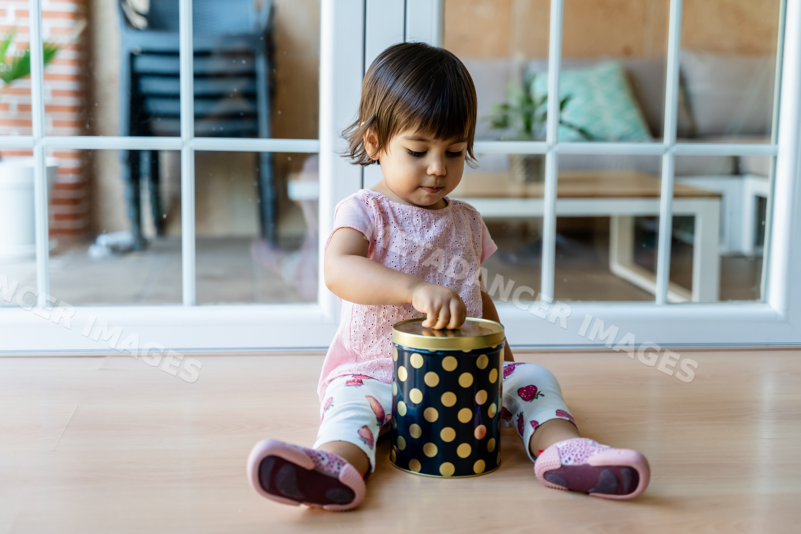Toddler white girl opening polka dot jar indoors on wooden floor