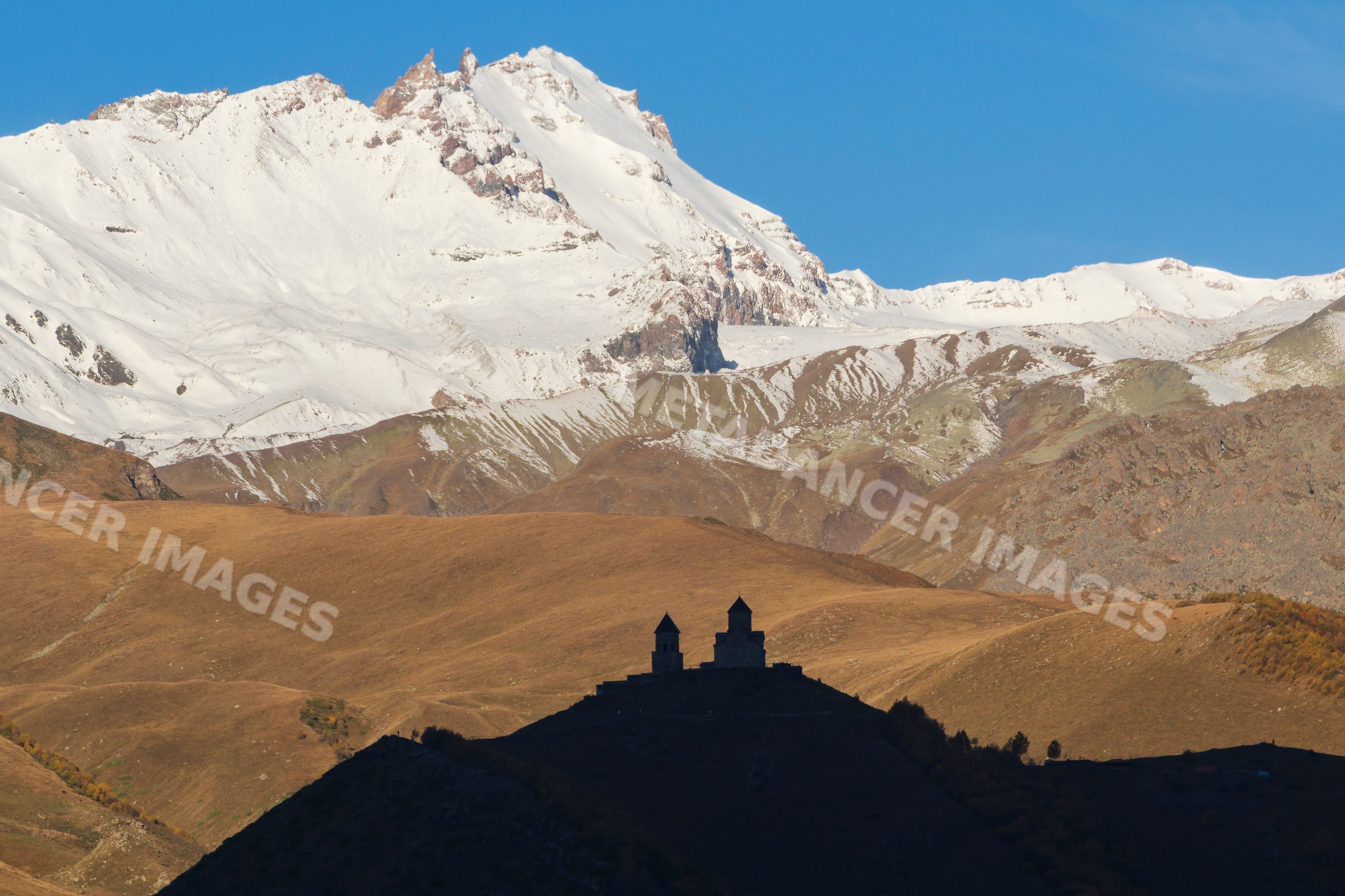Gergeti trinity church silhouette at Sunrise with snow mountains