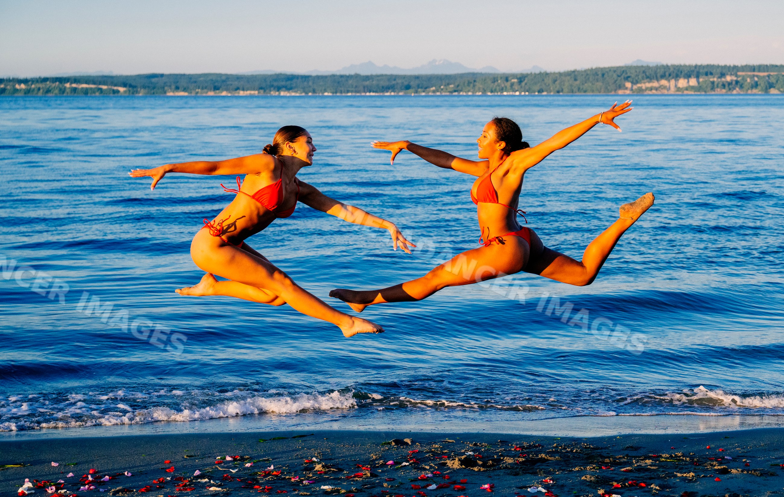Two women jump in unison on a beach shoreline in WA, USA