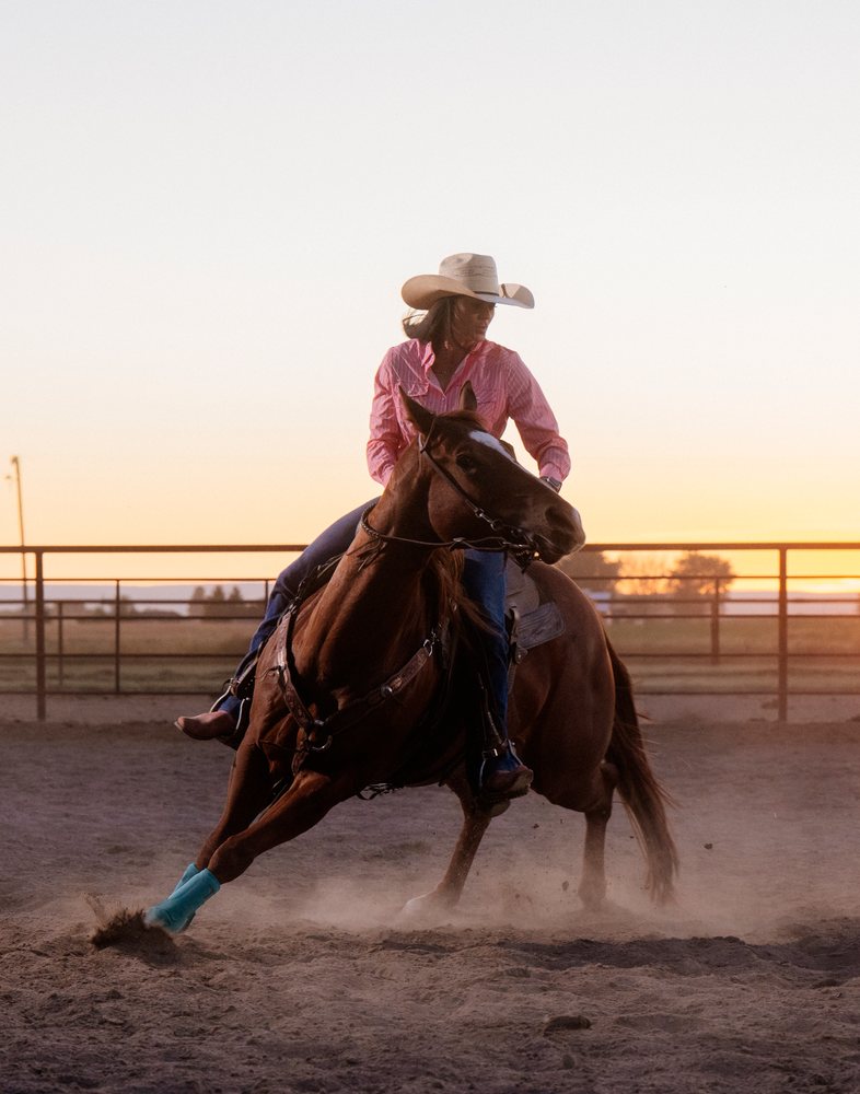 White woman riding brown horse in arena at sunset in Southwest USA
