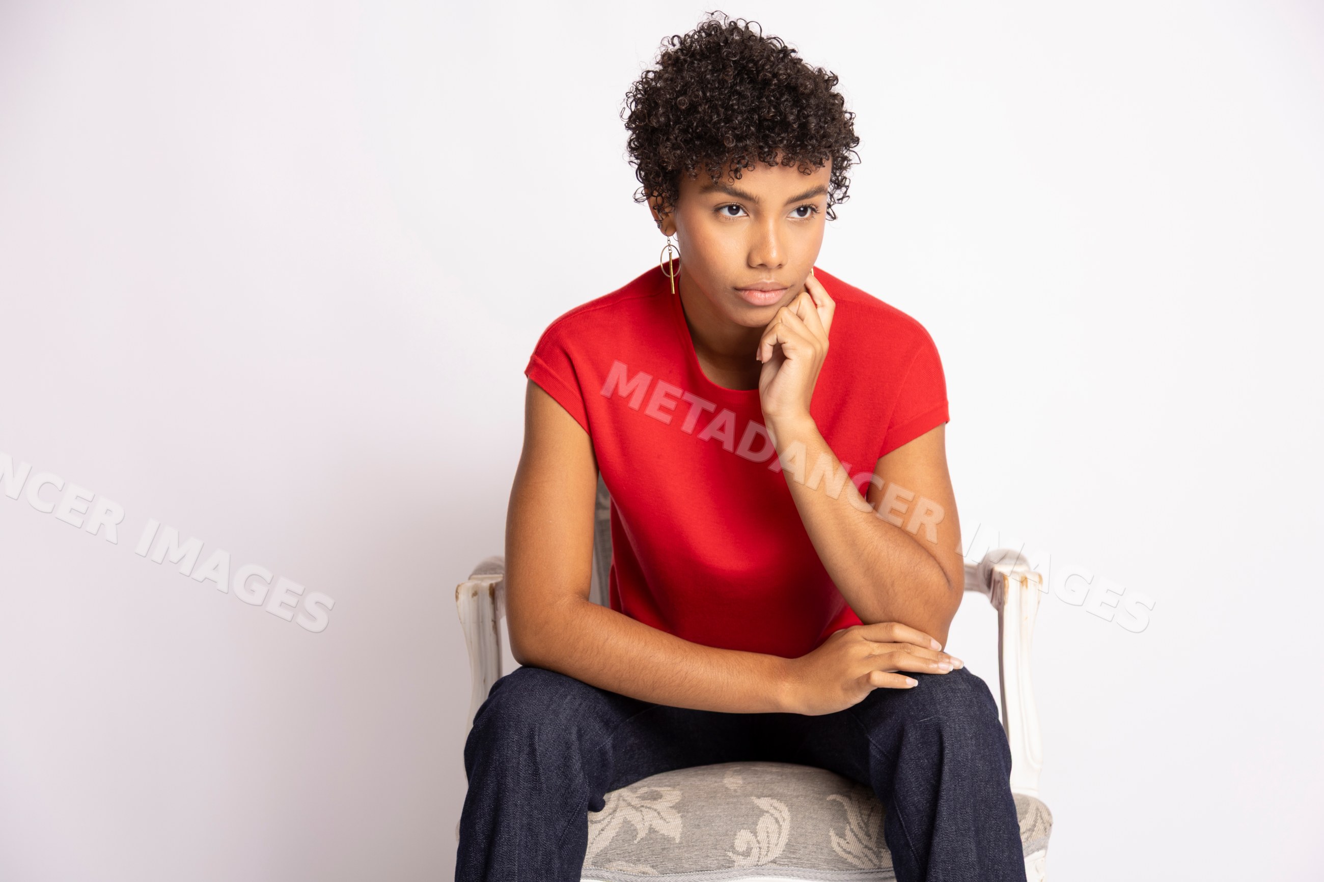 Young Hispanic woman seated thoughtfully in a red shirt in a studio