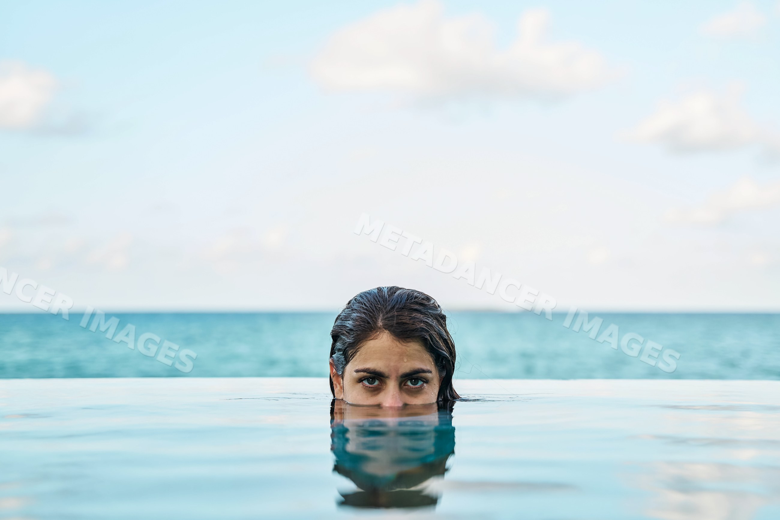 A white woman swimming in an infinity pool overlooking the ocean