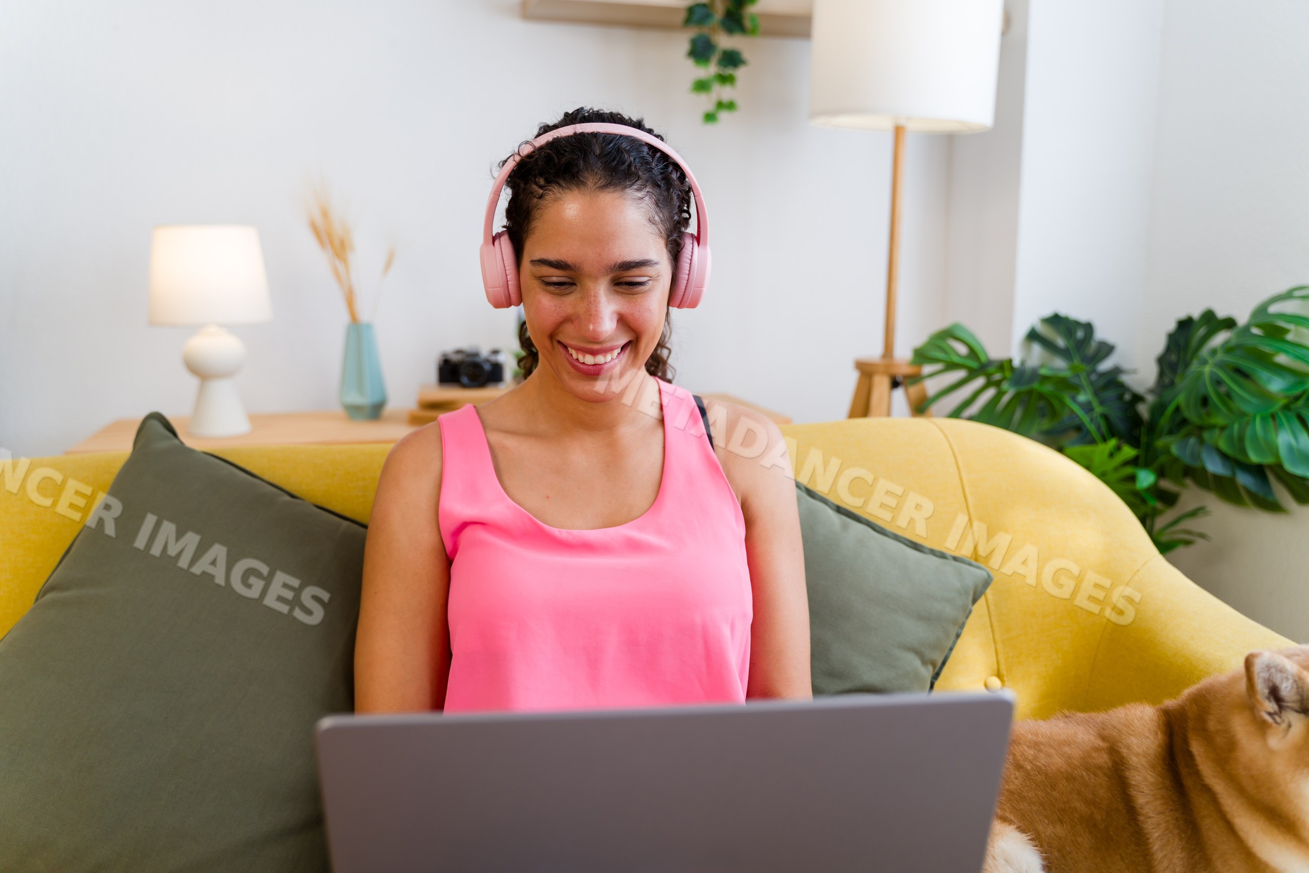 A Hispanic woman smiles while using a laptop on a yellow couch