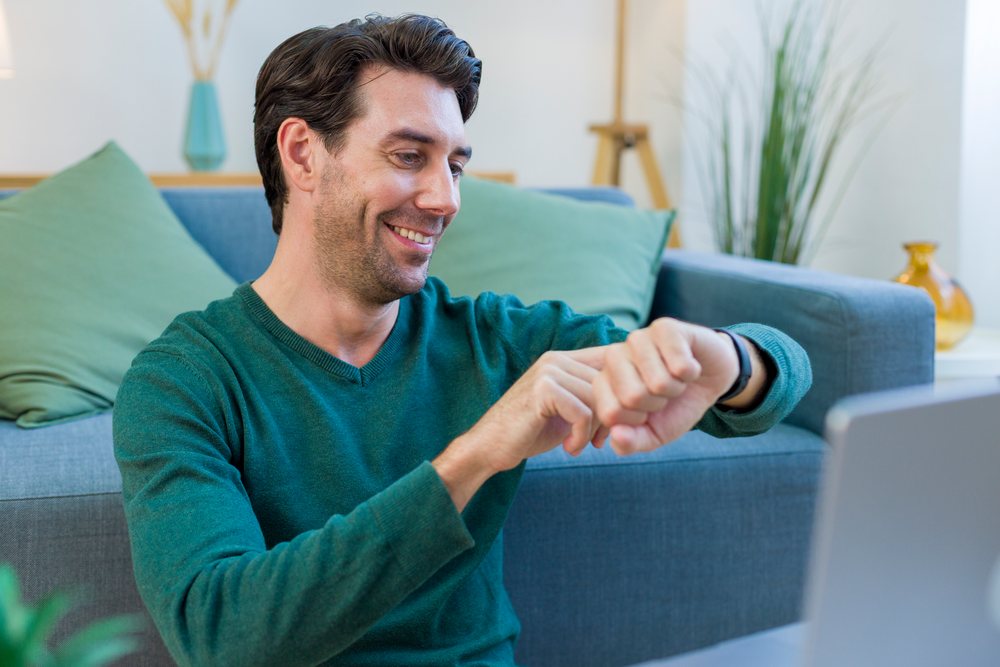 White man looking at watch while sitting on couch in living room