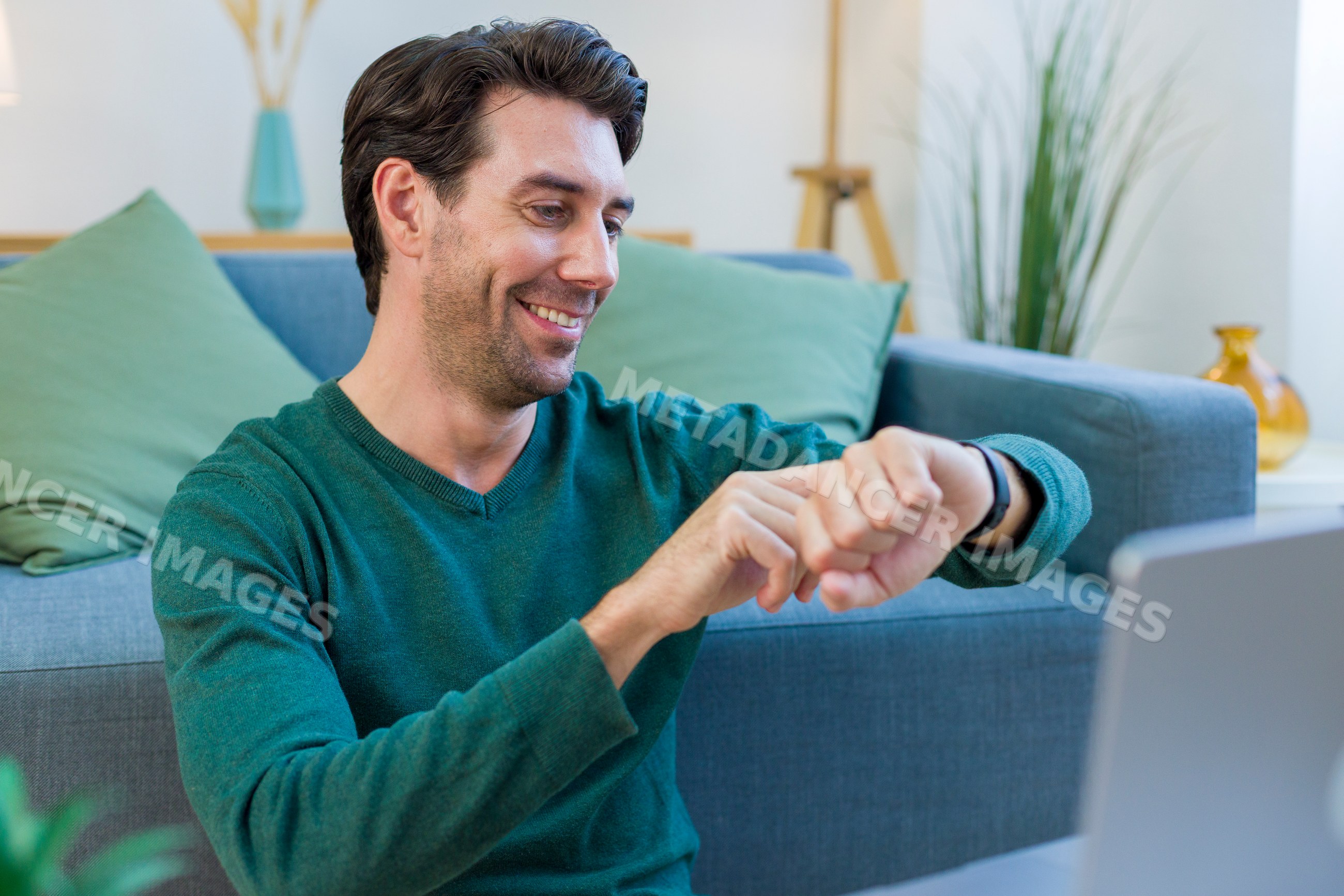 White man looking at watch while sitting on couch in living room