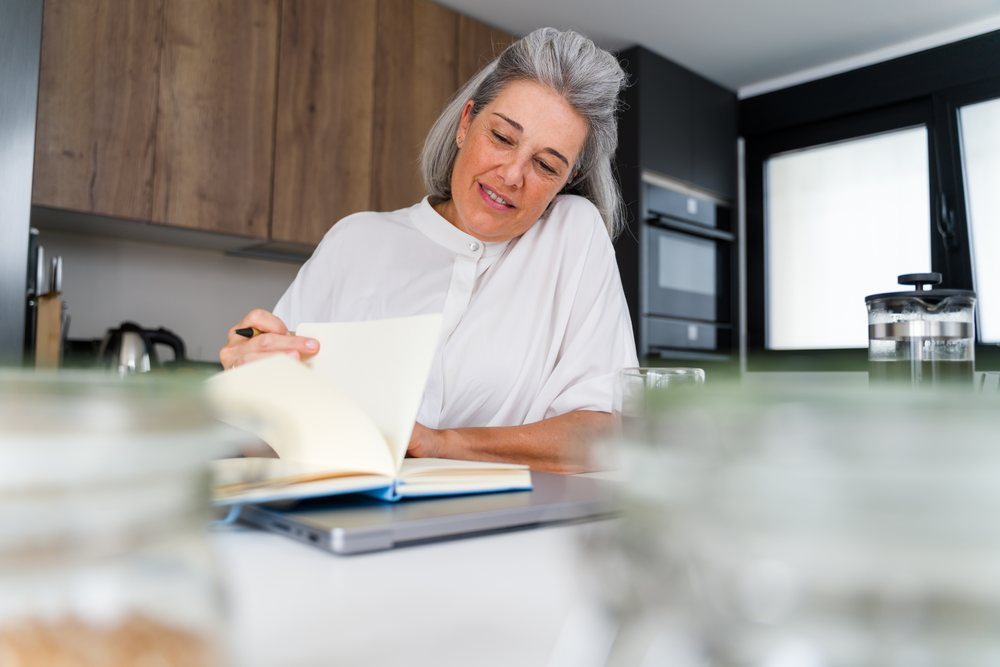 Middle-aged white woman reading and writing in modern kitchen in Spain