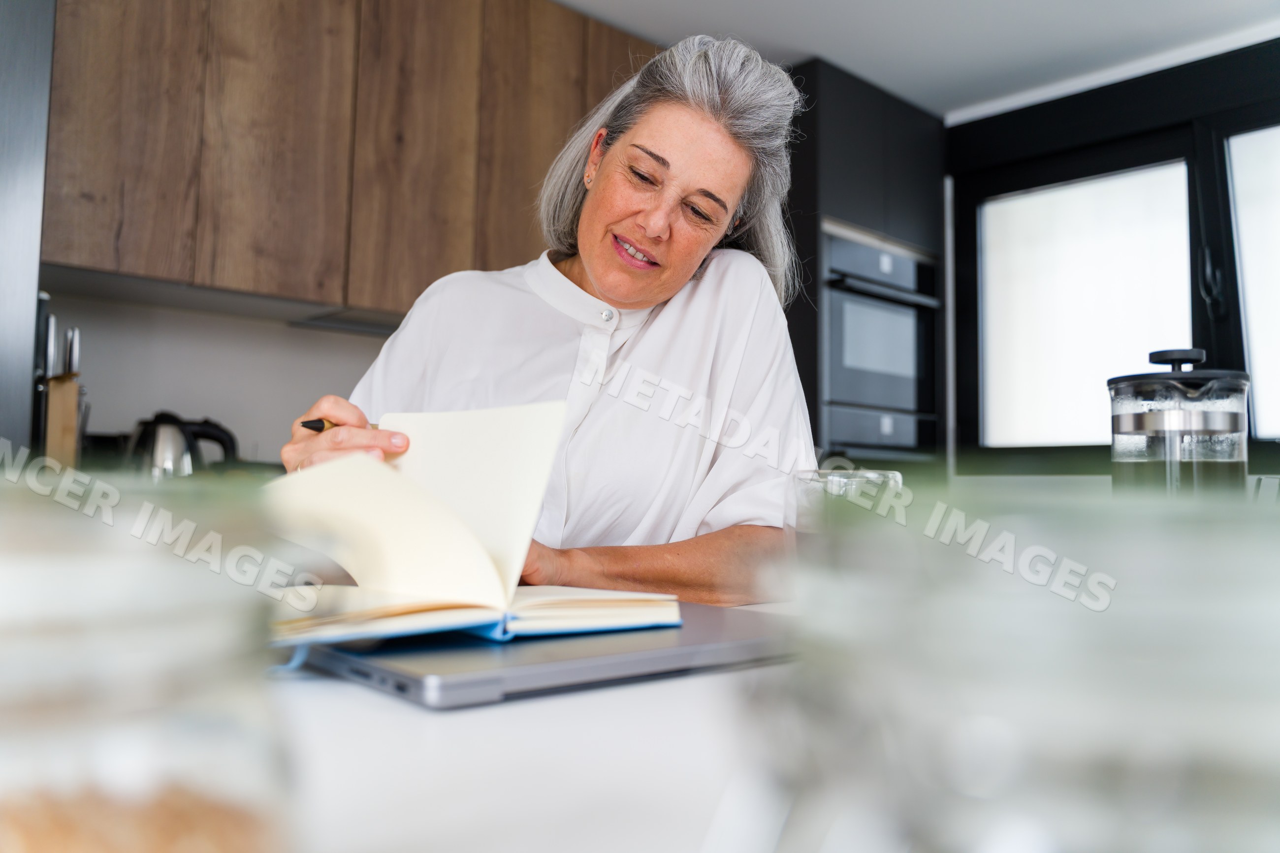 Middle-aged white woman reading and writing in modern kitchen in Spain
