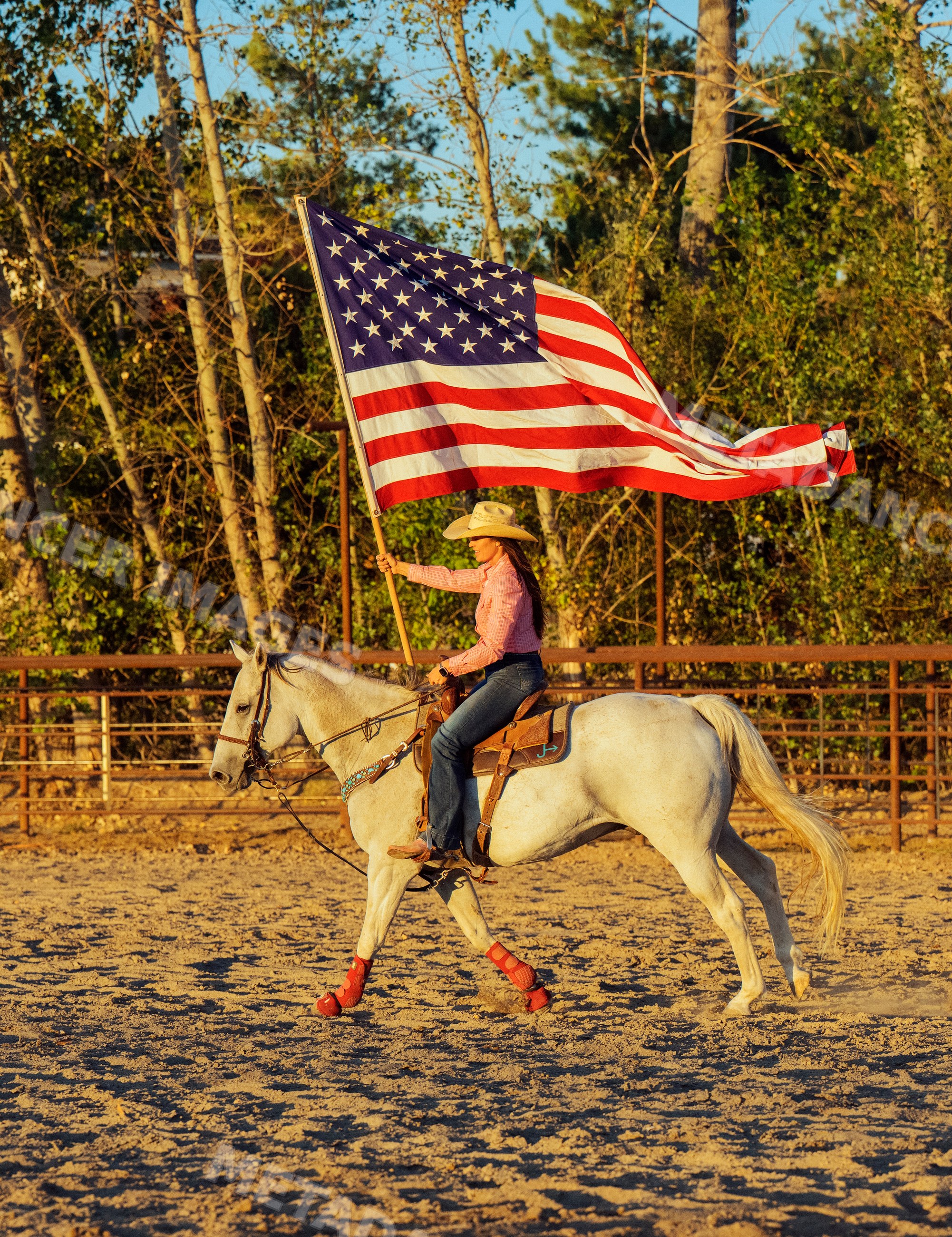 White woman on horseback carrying american flag in outdoor arena