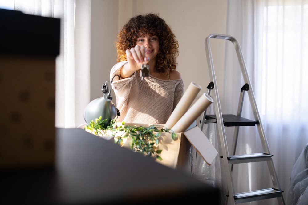 White woman holding keys beside cardboard box while moving indoors