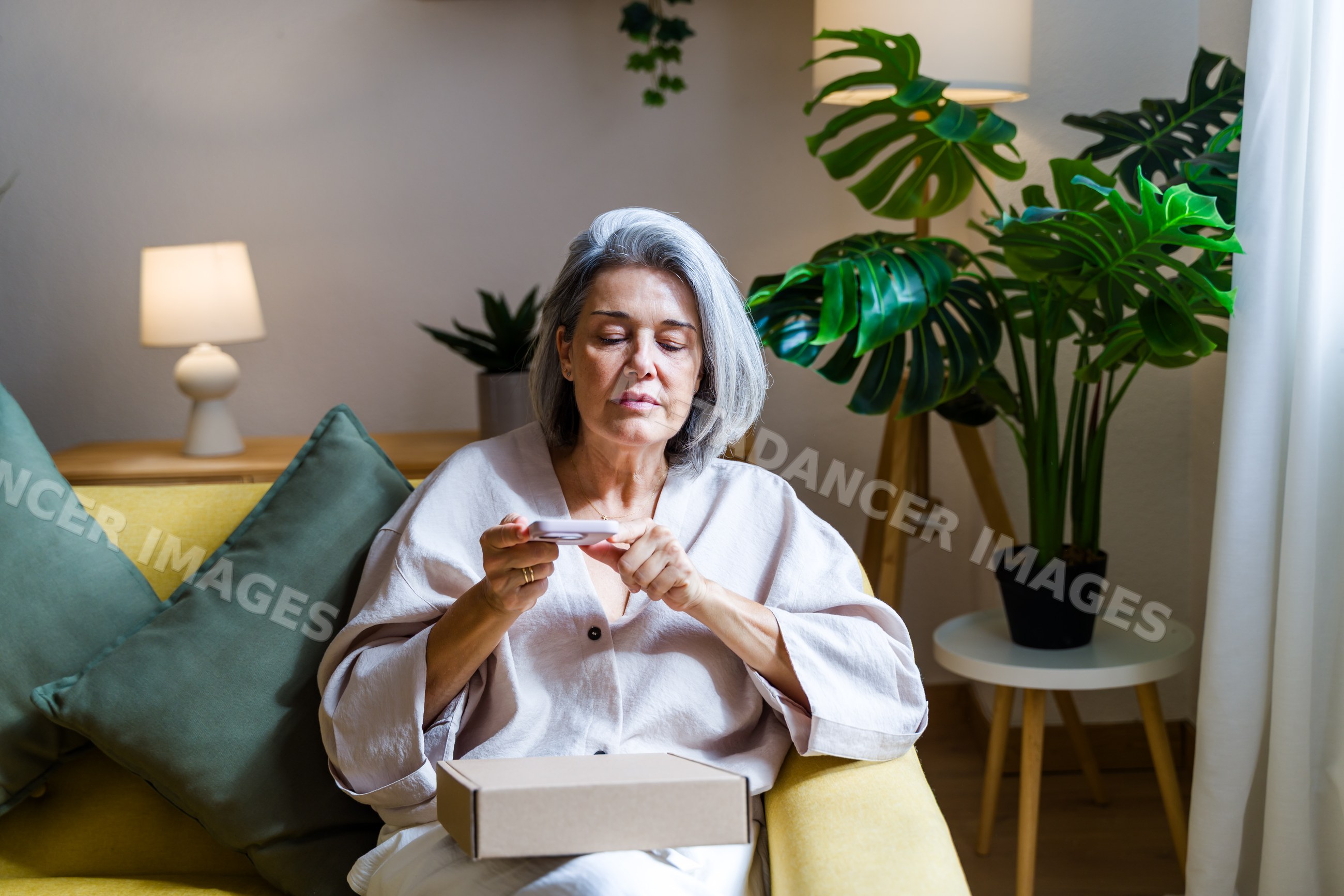 Middle-aged white woman using smartphone on yellow sofa