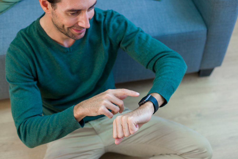 White man sitting on floor using smartwatch setting
