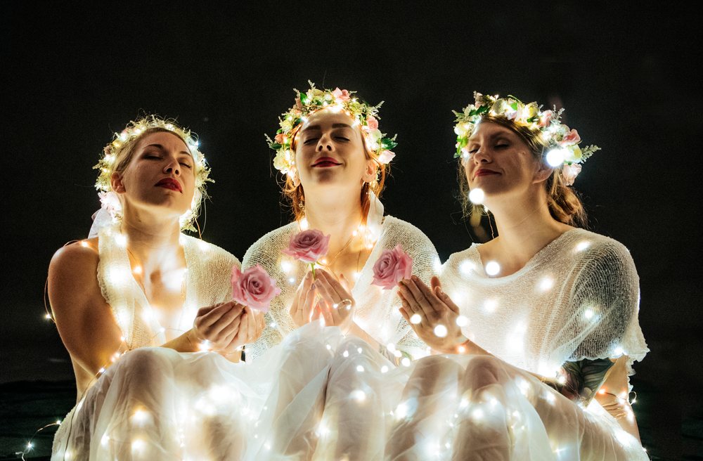 Three white women in flower crowns holding roses wrapped in glowing