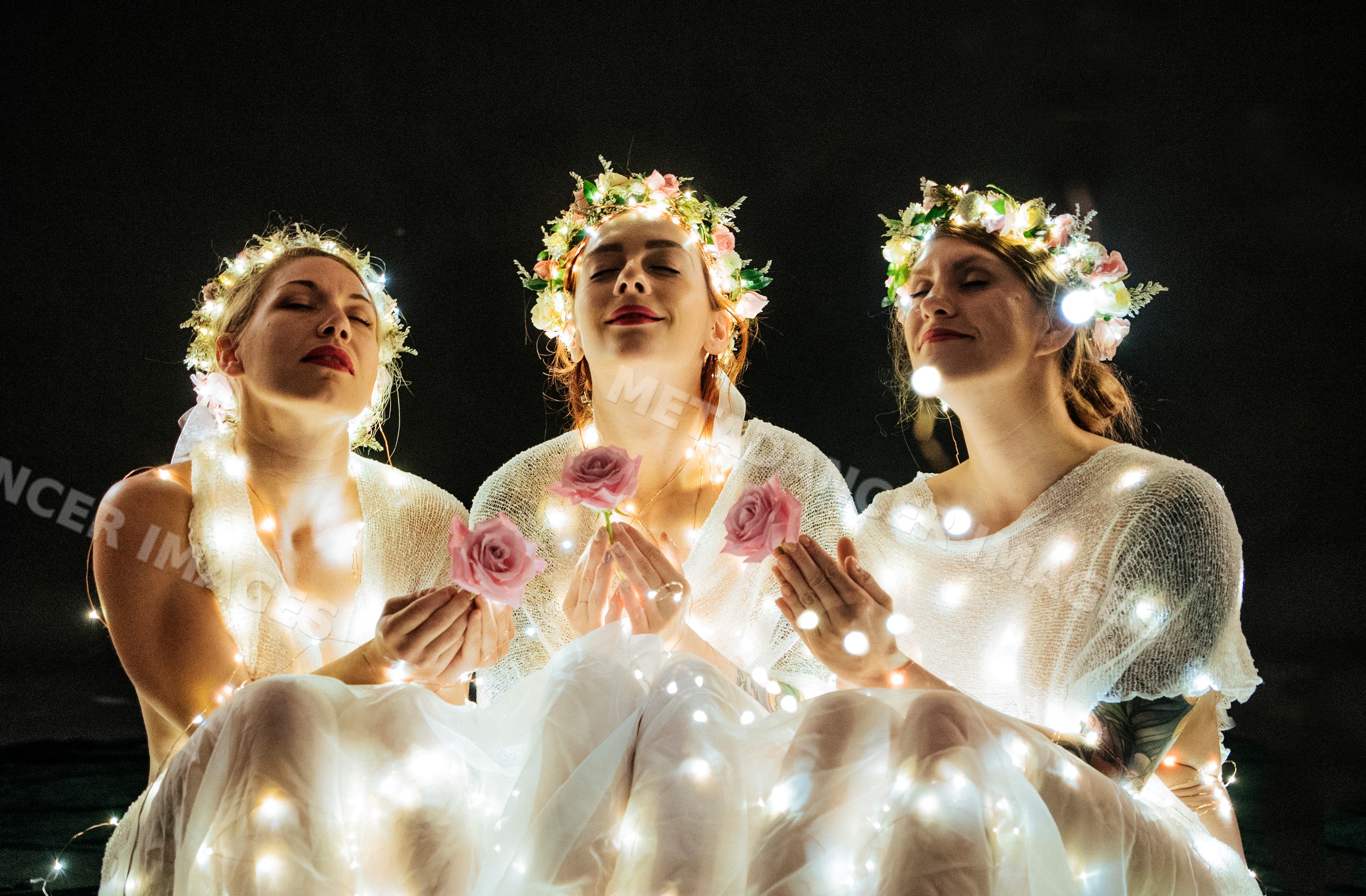Three white women in flower crowns holding roses wrapped in glowing