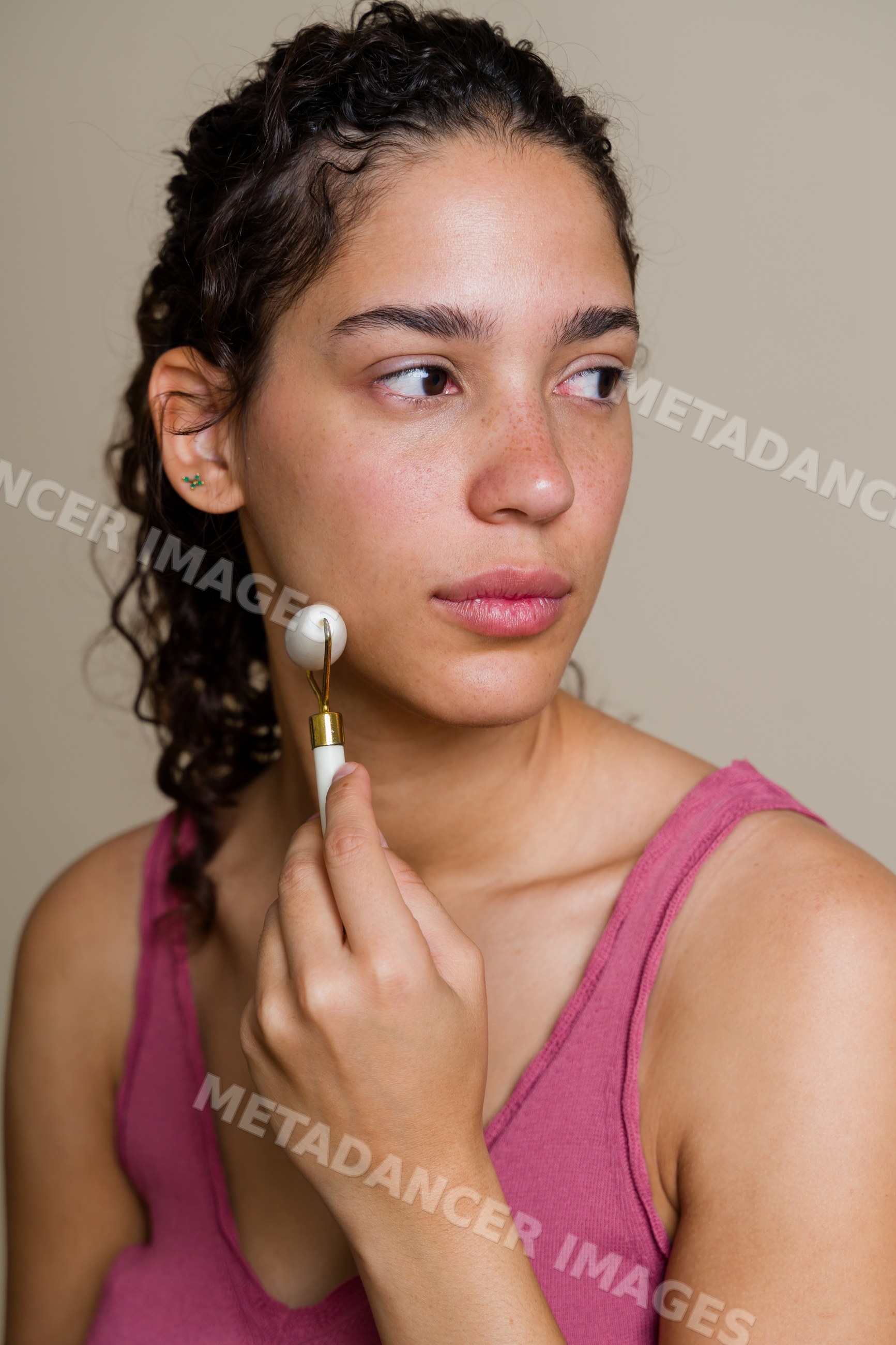 Hispanic woman massaging face with porcelain facial roller