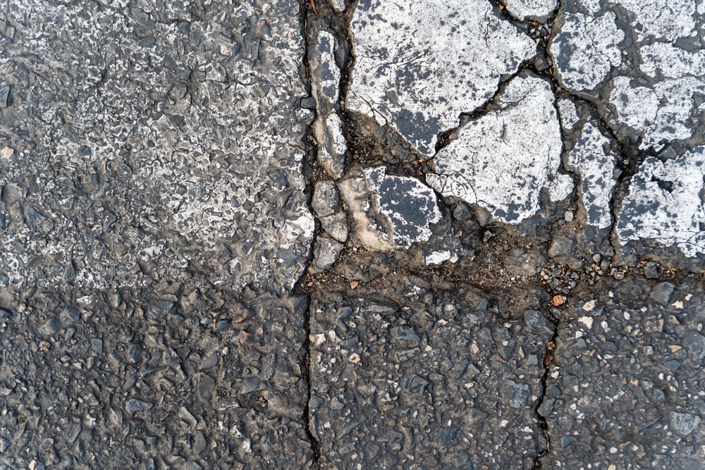 Cracked asphalt pavement with weathered stone aggregate texture