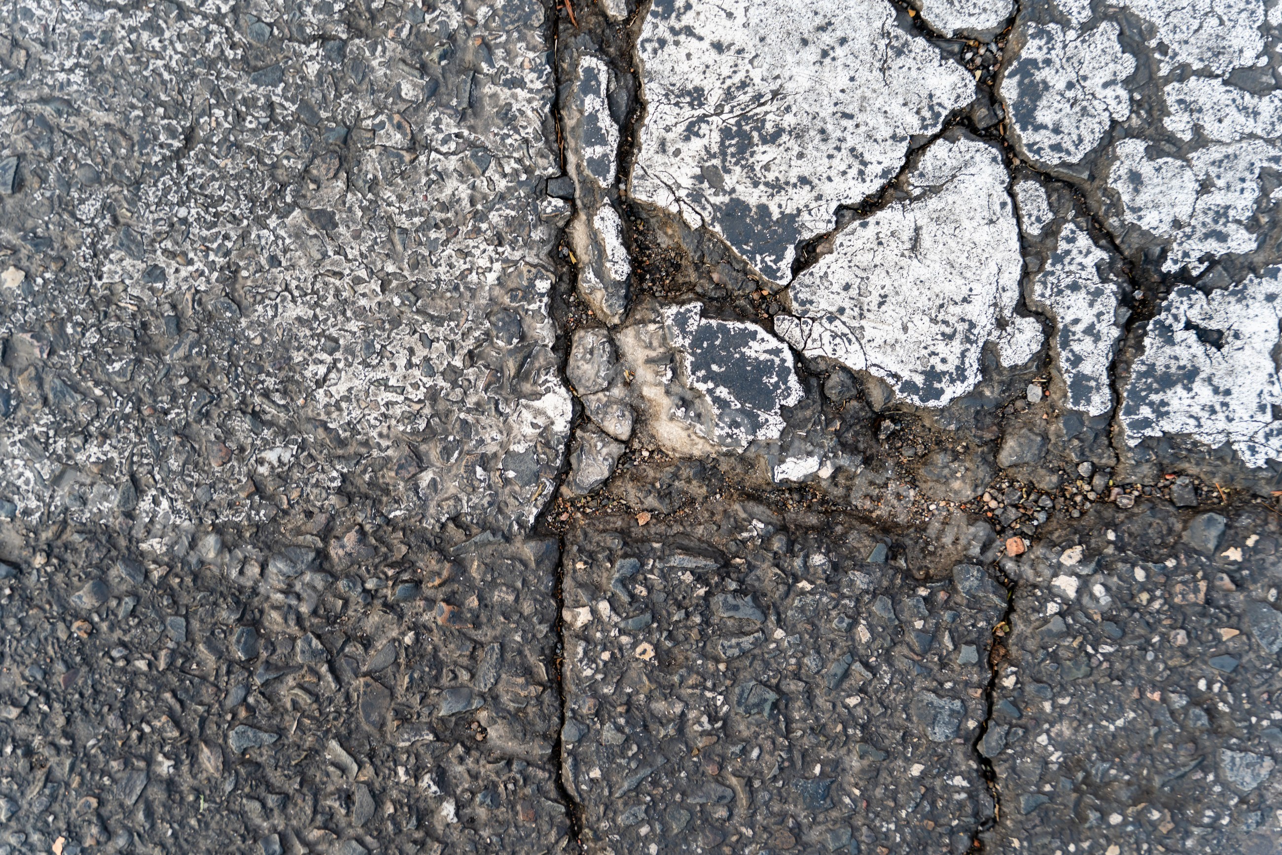 Cracked asphalt pavement with weathered stone aggregate texture